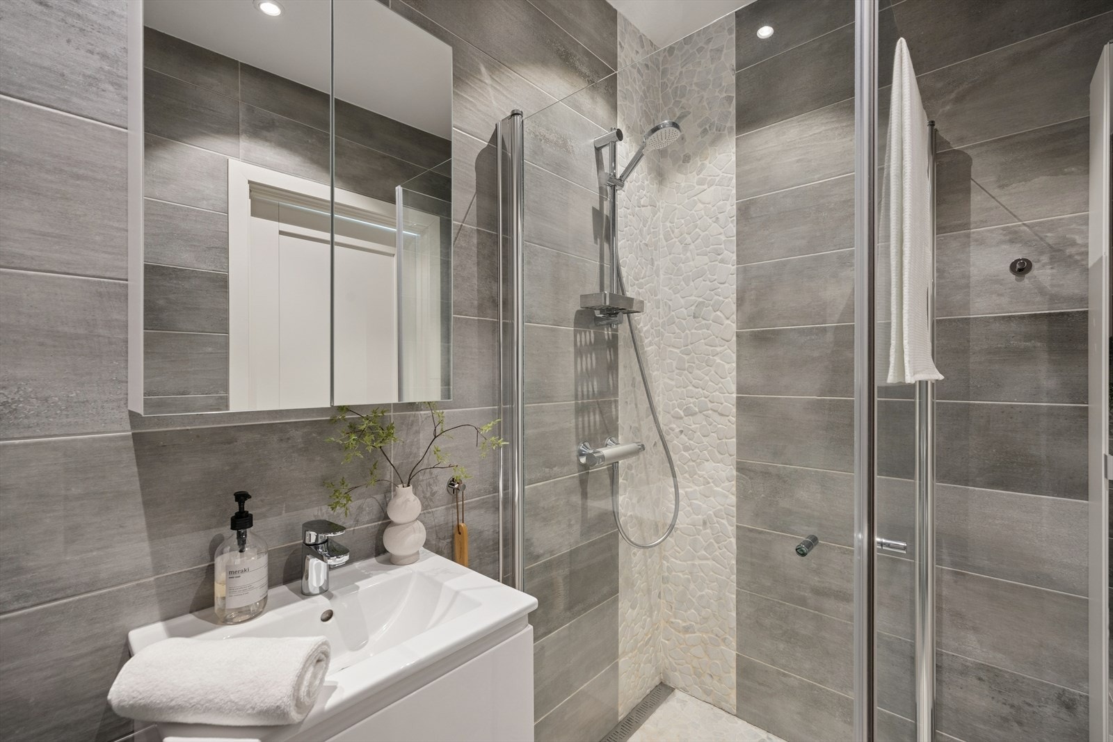 Rommet har innredning med nedfelt servant, veggmontert toalett med innebygget sisterne og dusj med innfellbare dører i herdet glass. Galleribilde