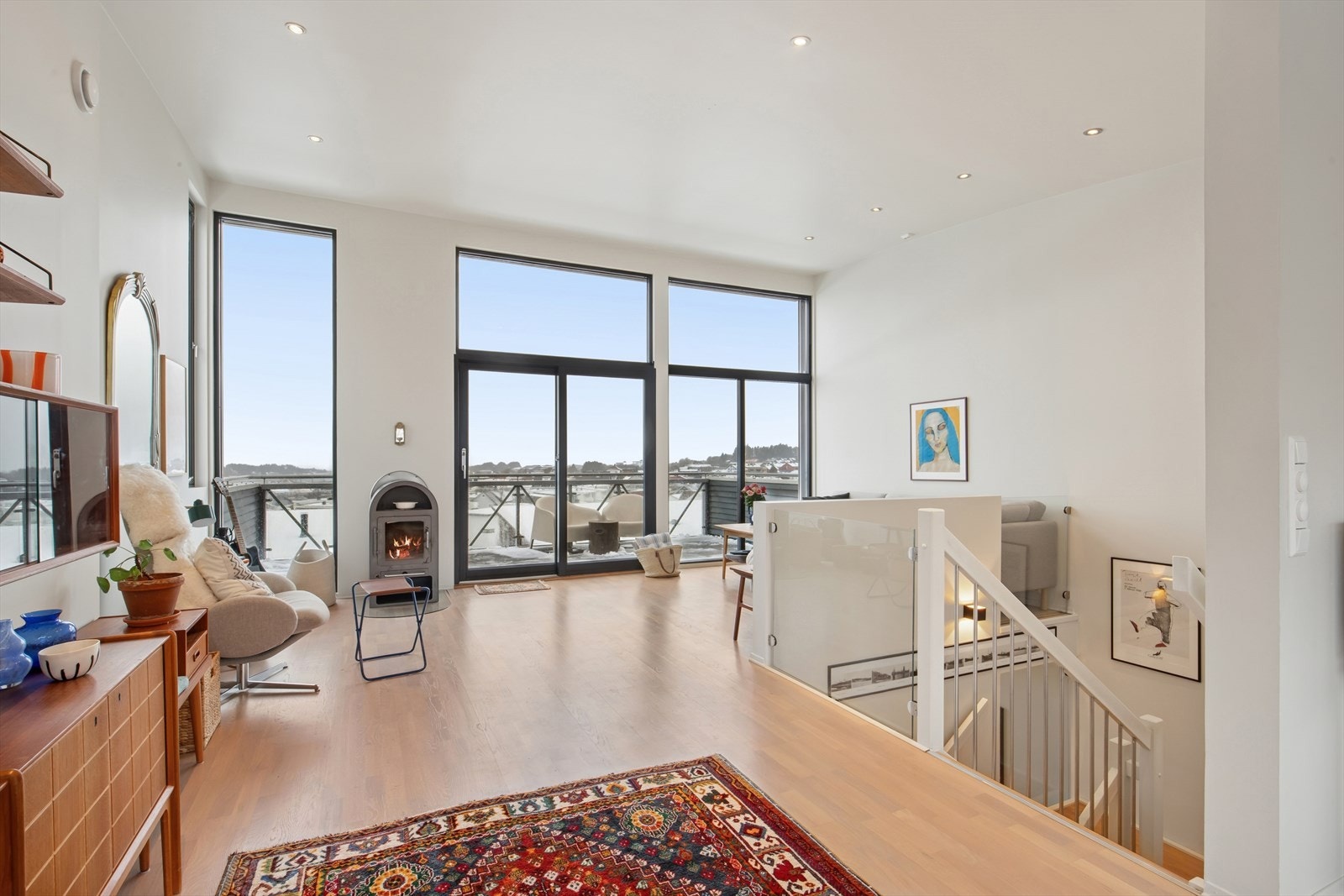 Luftig og stilfull stue med ekstra god takhøyde, store vindusflater og direkte utgang til balkong. Vedovn, gjennomgående lys og moderne materialvalg skaper en varm og behagelig atmosfære. Galleribilde