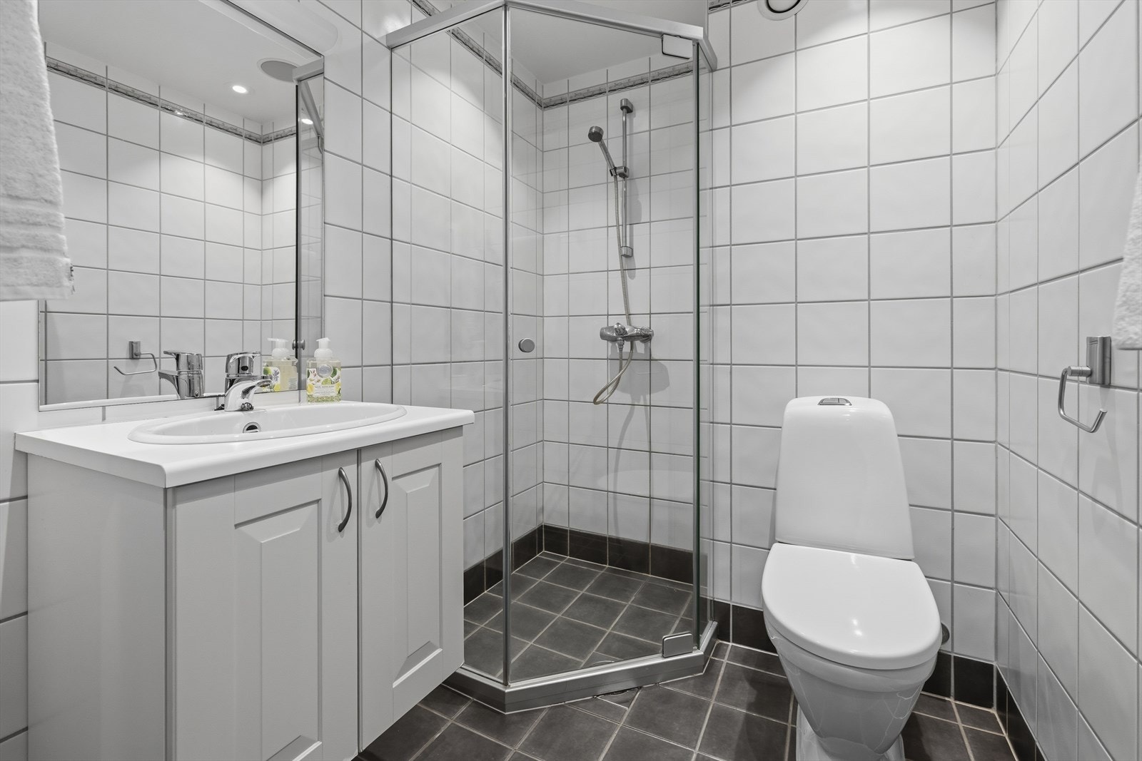 Bad/wc 1 med flislagt gulv med varmekabler. Badet har dushjørne, toalett, servantskap og servant med blandebatteri. Flislagte vegger og malte plater i himling Galleribilde