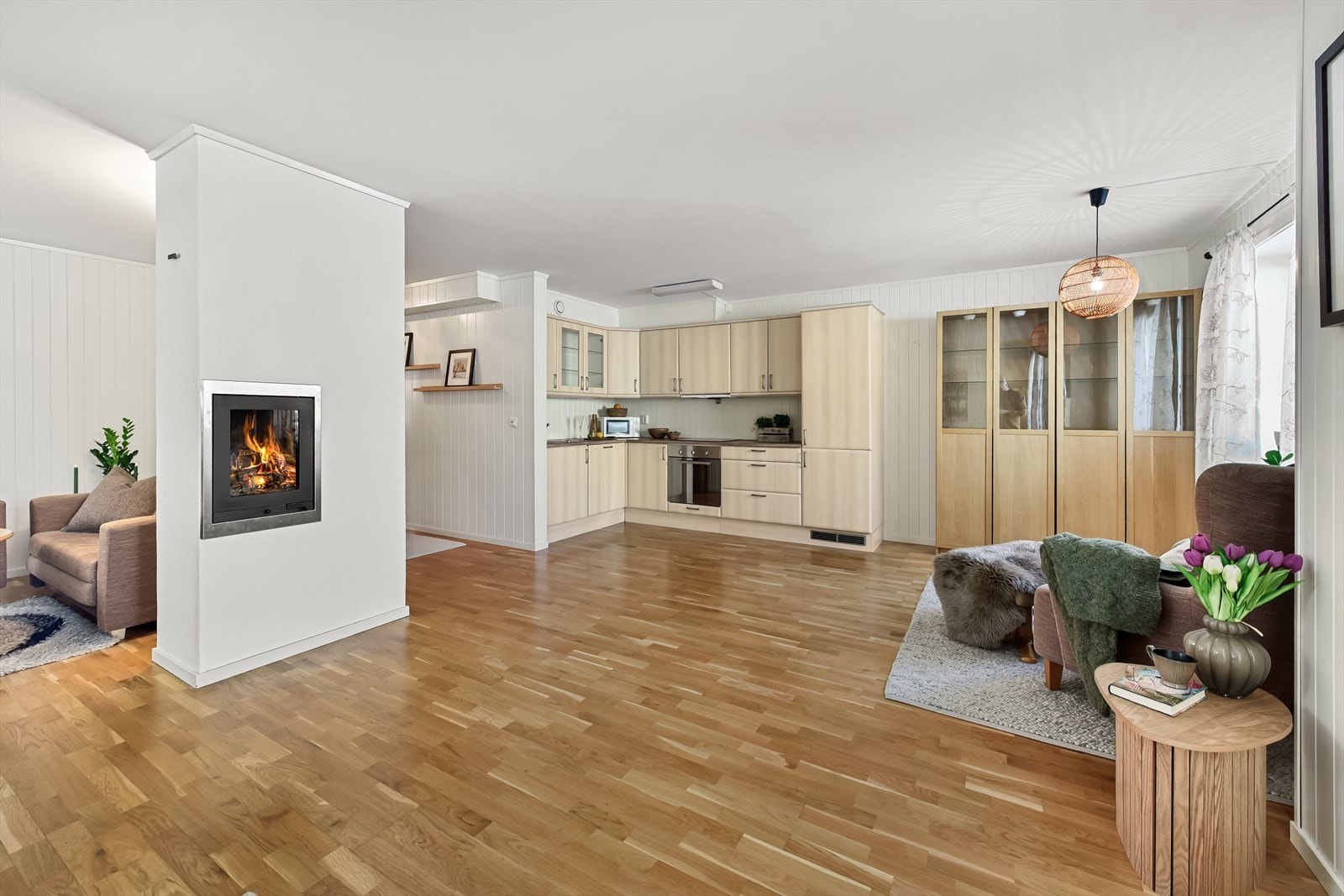 En åpen og sosial planløsning mellom stue og kjøkken, med en sentralt plassert peisinnsats. Galleribilde