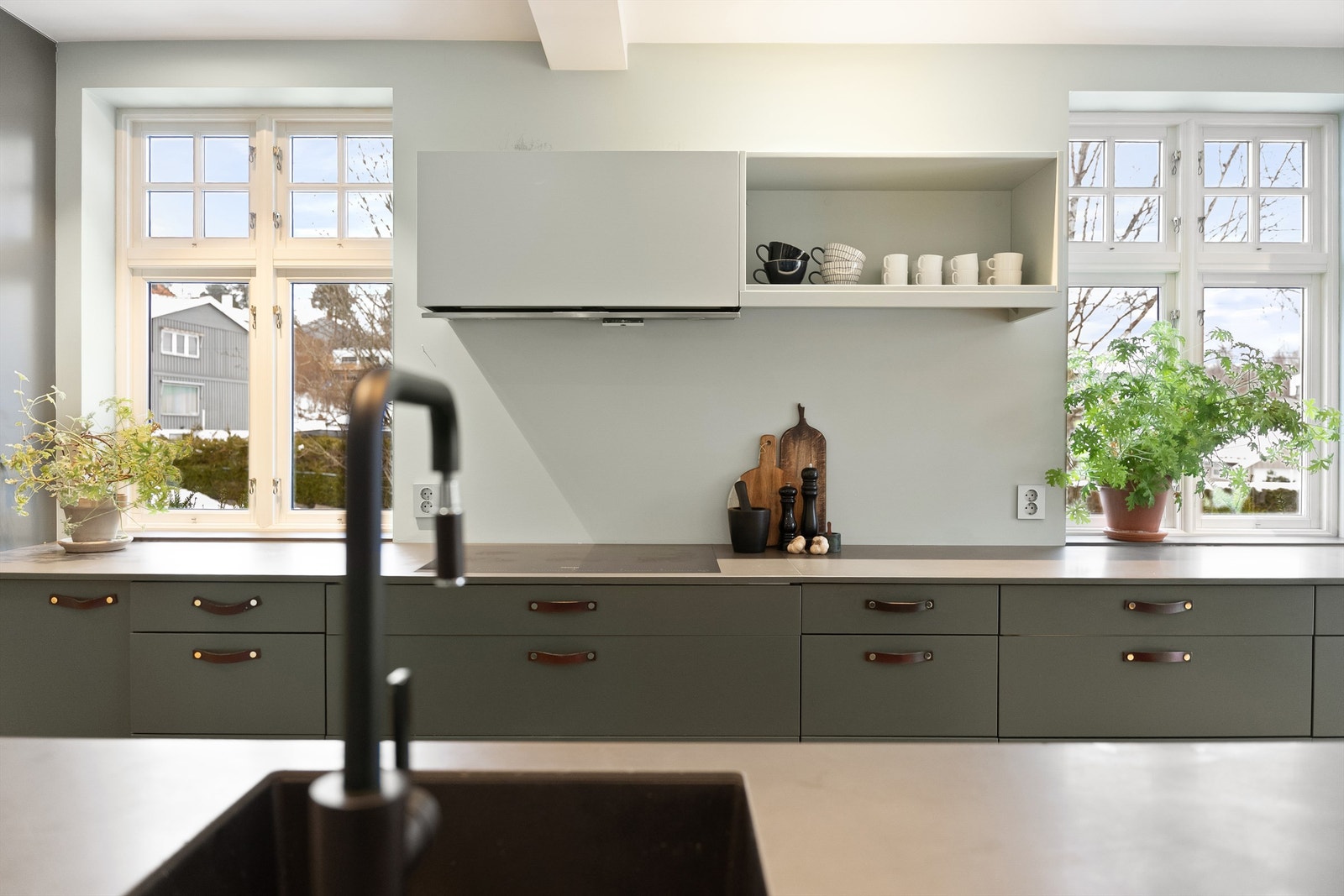 Store vindusflater over arbeidsbenken gir rikelig med naturlig lys. Merk også den plassbyggete hyllen over induksjonstoppen. Galleribilde