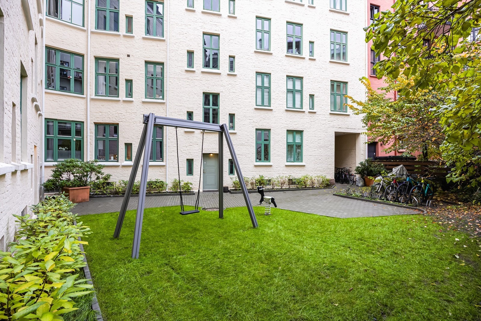 Grønn felles bakgård som er opparbeidet med blant annet steinsatte arealer, grøntområde, lekeapparater og diverse beplantninger. Galleribilde