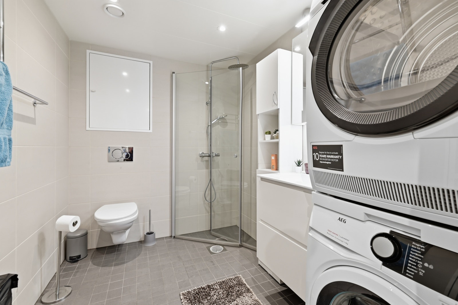 Pent flislagt bad med toalett, servant, hjørnedusj, tørketrommel og vaskemaskin. Galleribilde