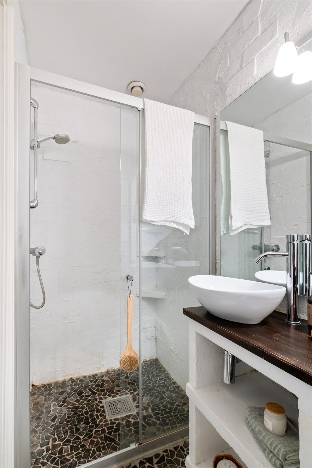 Badet er innredet med en servant, overhengende speil og belysning. Dusjen er plassert i hjørnet og har håndholdt dusjarmatur samt dusjvegger. Videre er det montert et gulvstående toalett. Galleribilde