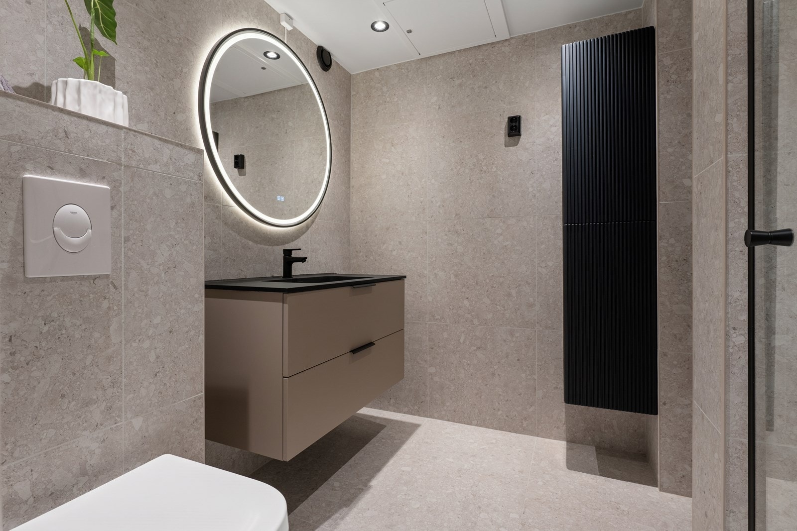 Rommet er innredet med servantskap med servant og speil med integrert belysning, vegghengt toalett med innebygget sisterne og en vegghengt dusj med skjermdør i herdet glass. Galleribilde