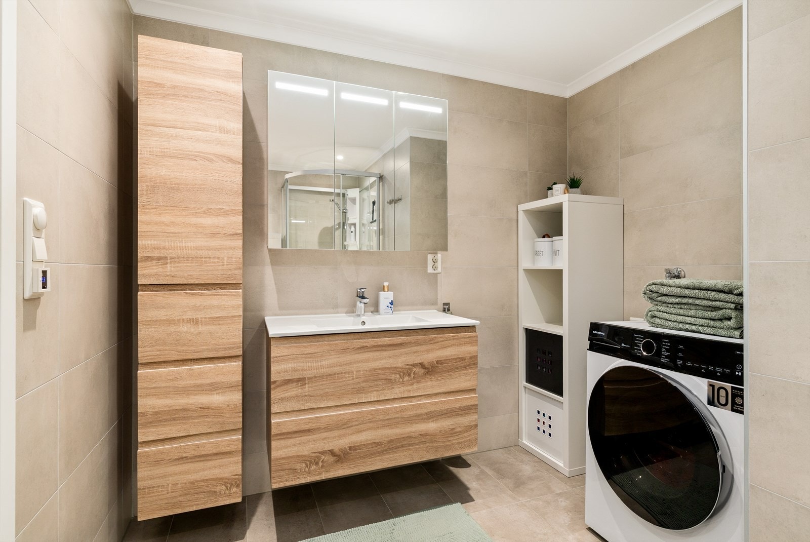 Badet er innredet med nedfelt servant, veggmontert toalett, dusjkabinett og opplegg for vaskemaskin. Galleribilde