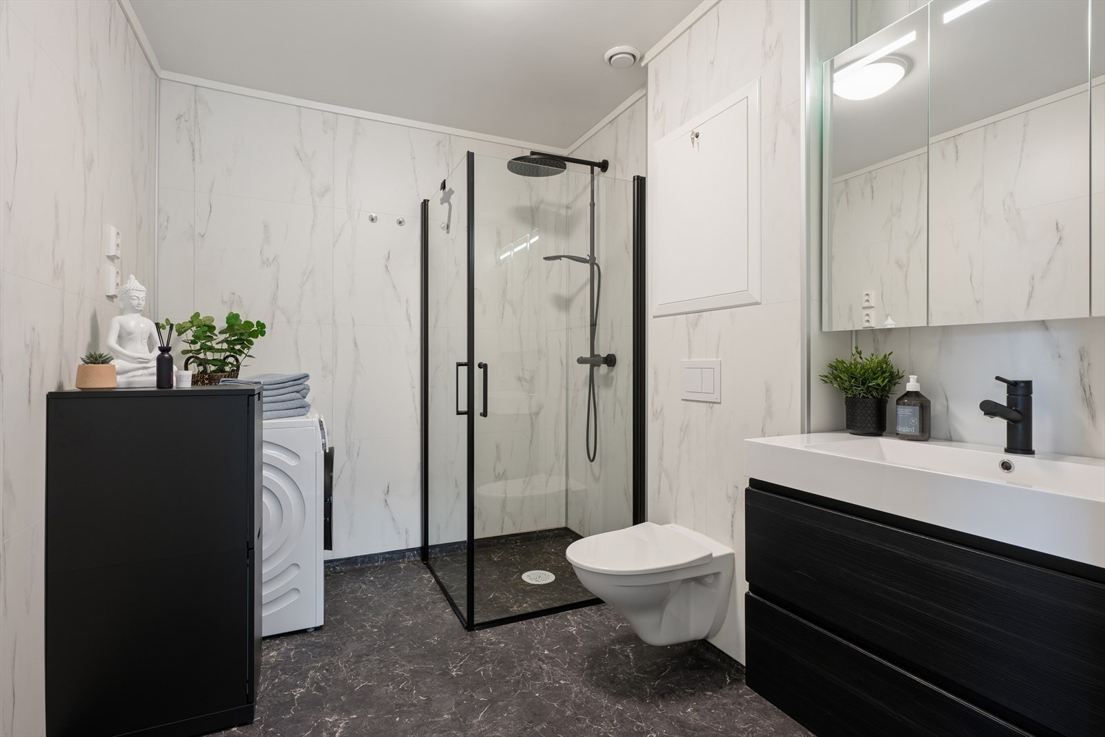 Rommet er innredet med servant med underskap, speil med belysning, dusjvegger, vegghengt toalett og vaskemaskin. Galleribilde