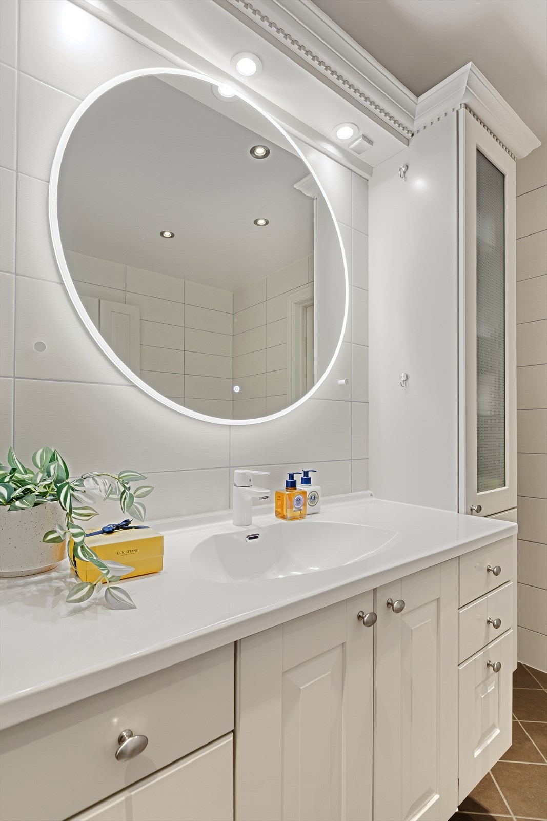 Godt vedlikeholdt baderomsinnredning, med moderne rundt speil med lys. Galleribilde