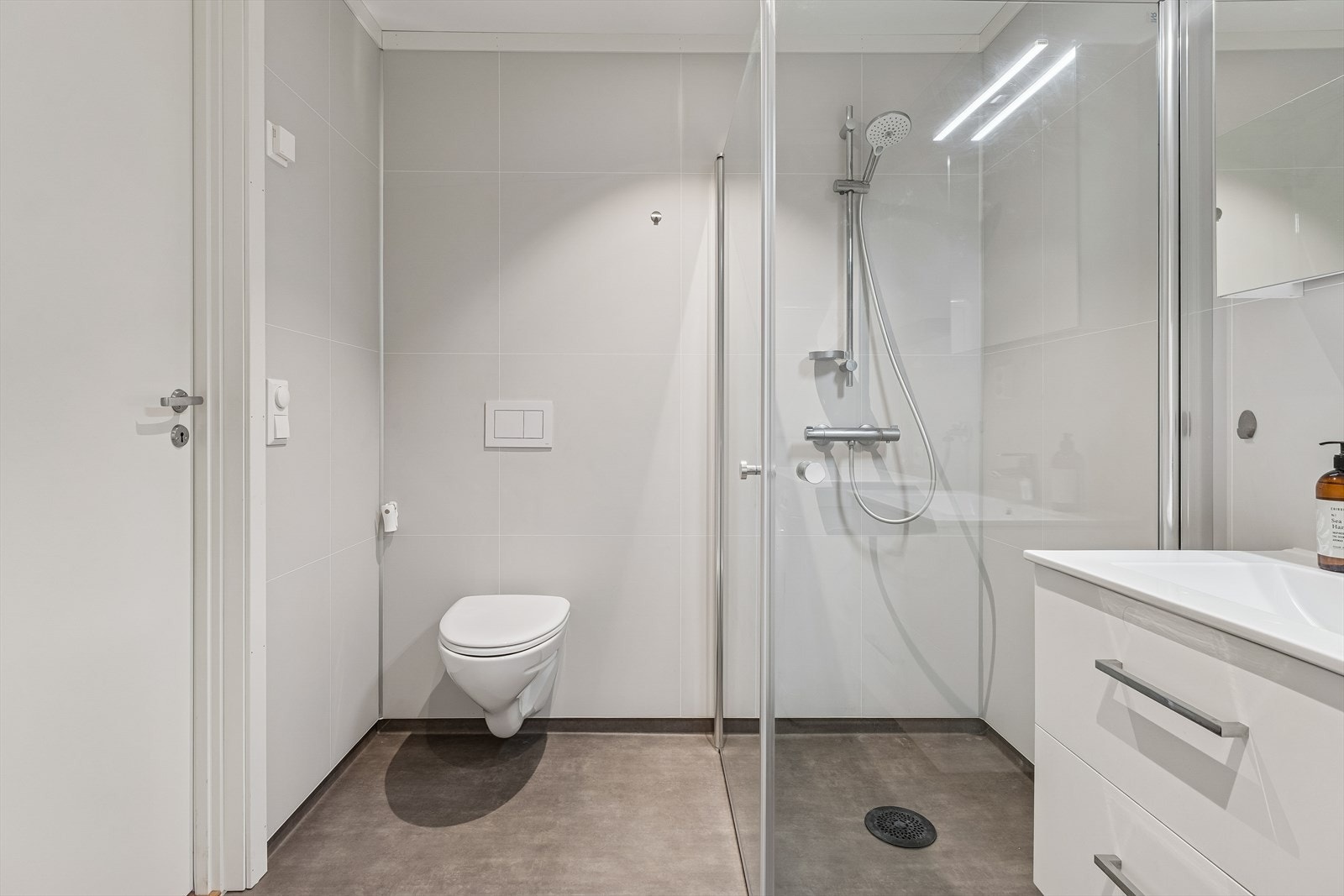 Badet er moderne med vegghengt toalett, dusjdører i glass og baderomsplater på veggene. Galleribilde