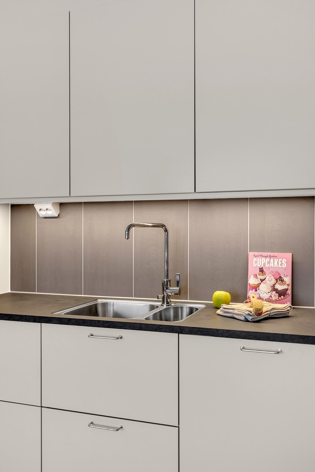 Kjøkkeninnredning bestående av laminert benkeplate, benkeskapsbelysning, stikkontakter, oppvaskkum av rustfritt stål med ett-greps armatur og integrerte hvitevarer. Galleribilde