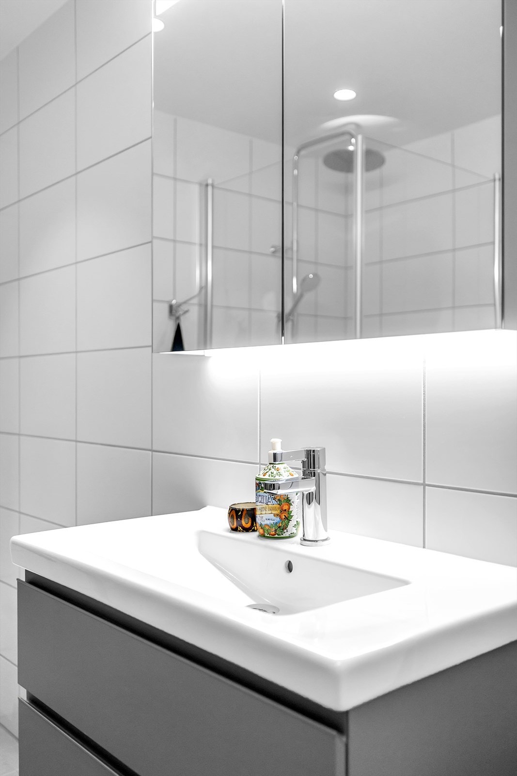 Baderomsinnredning bestående av vegghengt servantskap, heldekkende servant og ett-greps armatur, overskap med speildører, dusjnisje med innfellbare glassdører, regnfallsdusj, dusjarmatur og vegghengt toalett. Galleribilde