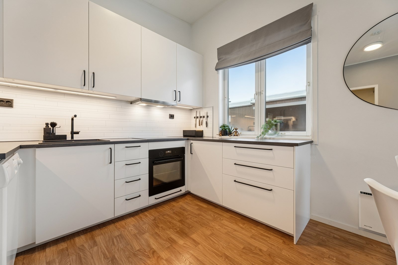 Kjøkkenet fremstår moderne og tiltalende med hvite, glatte fronter og en benkeplate i laminat som kombinerer både stil og funksjonalitet. Galleribilde