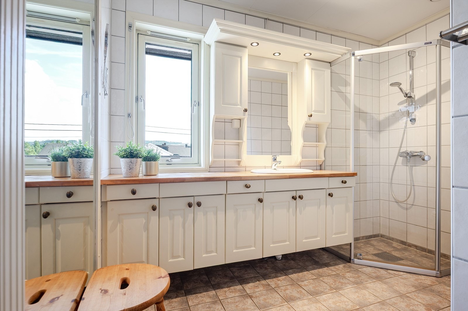 Badet med flislagt gulv, hjørnedusj, servant, toalett og mye skapplass. Galleribilde