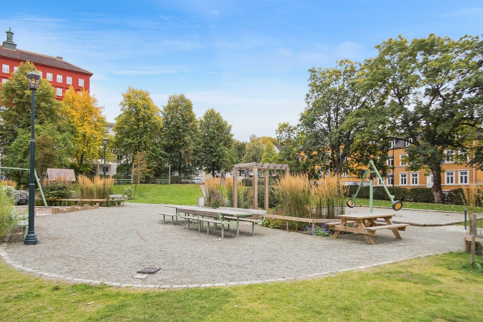 Trivelig uteområde bak Bispehaugen skole med sitteplasser, lekeapparater, grønn plen og store trær som skaper rolige og hyggelige omgivelser. Galleribilde
