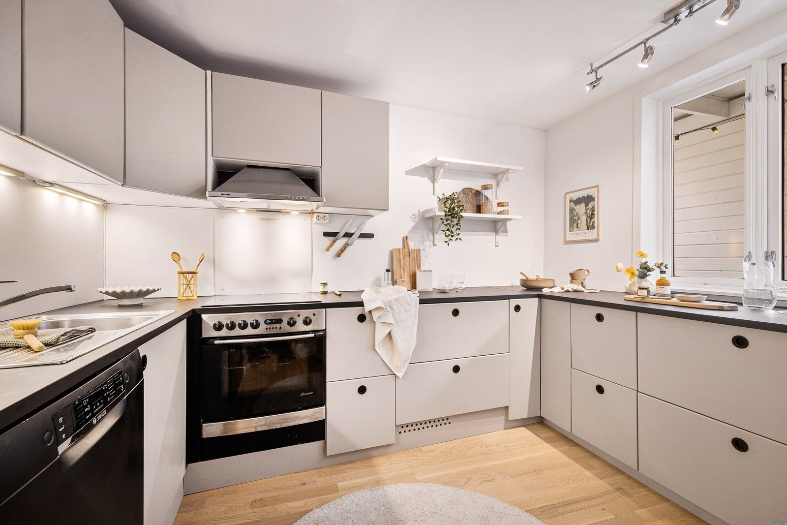 Flott kjøkken i grå utførelse med sort laminat benkeplate samt lys og strømuttak under overskap. Galleribilde