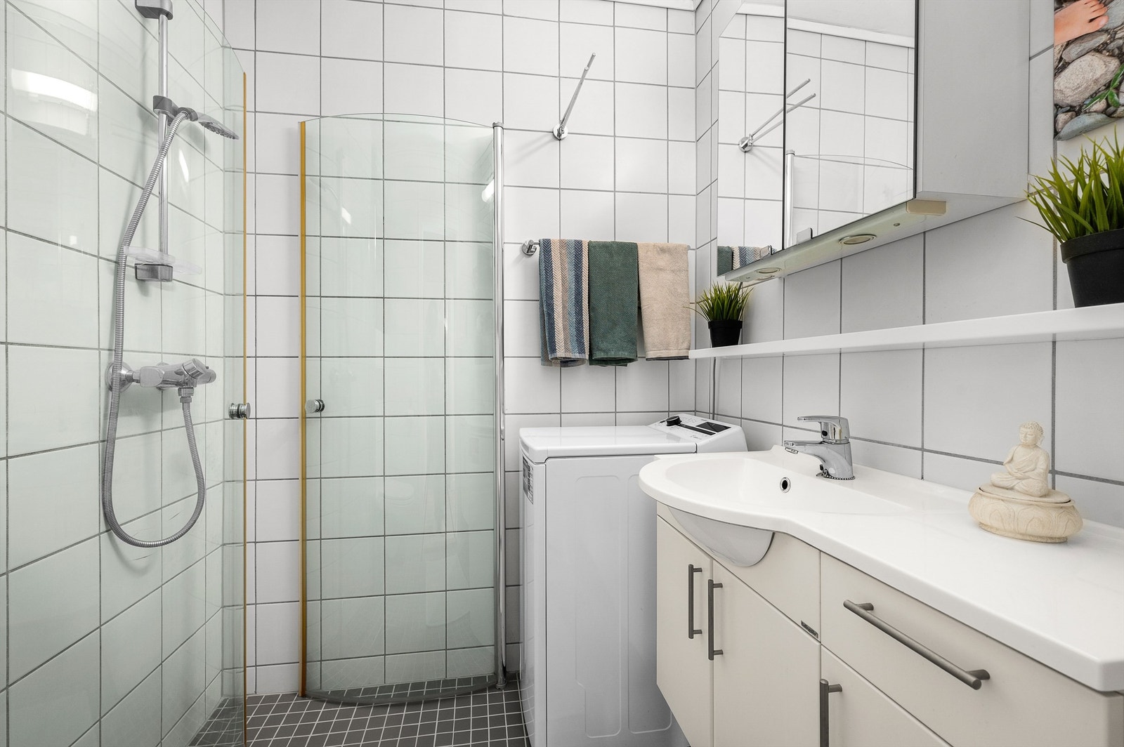 Pent flislagt bad på 2,5 kvm med gulvvarme og opplegg for vaskemaskin. Videre er badet innredet med servantskap med overskap med speil og lys, dusjhjørne og vegghengt toalett. Galleribilde