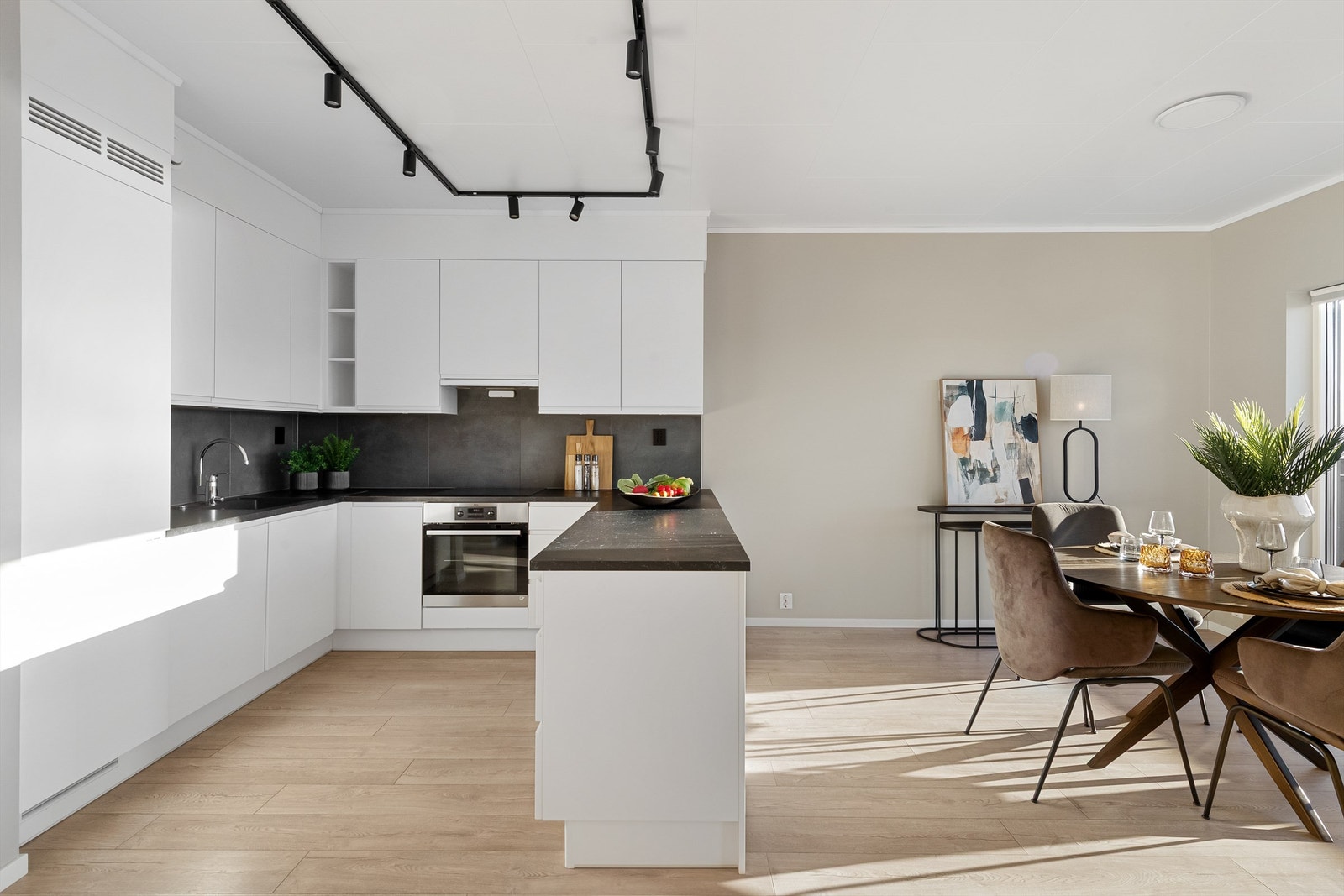 Hvit kjøkkeninnredning med underskap og takhøye overskap, glatte fronter. "Kjøkkenøy"/benk mot spiseplassen. Galleribilde