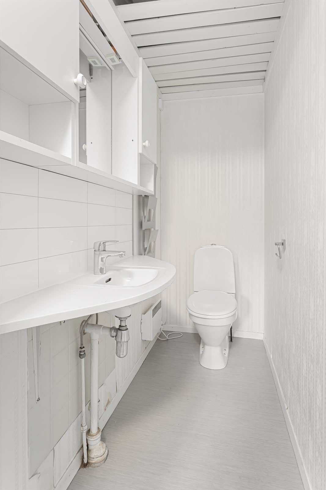 Praktisk toalettrom innredet med vegghengt servant, gulvstående toalett og overskap. Galleribilde