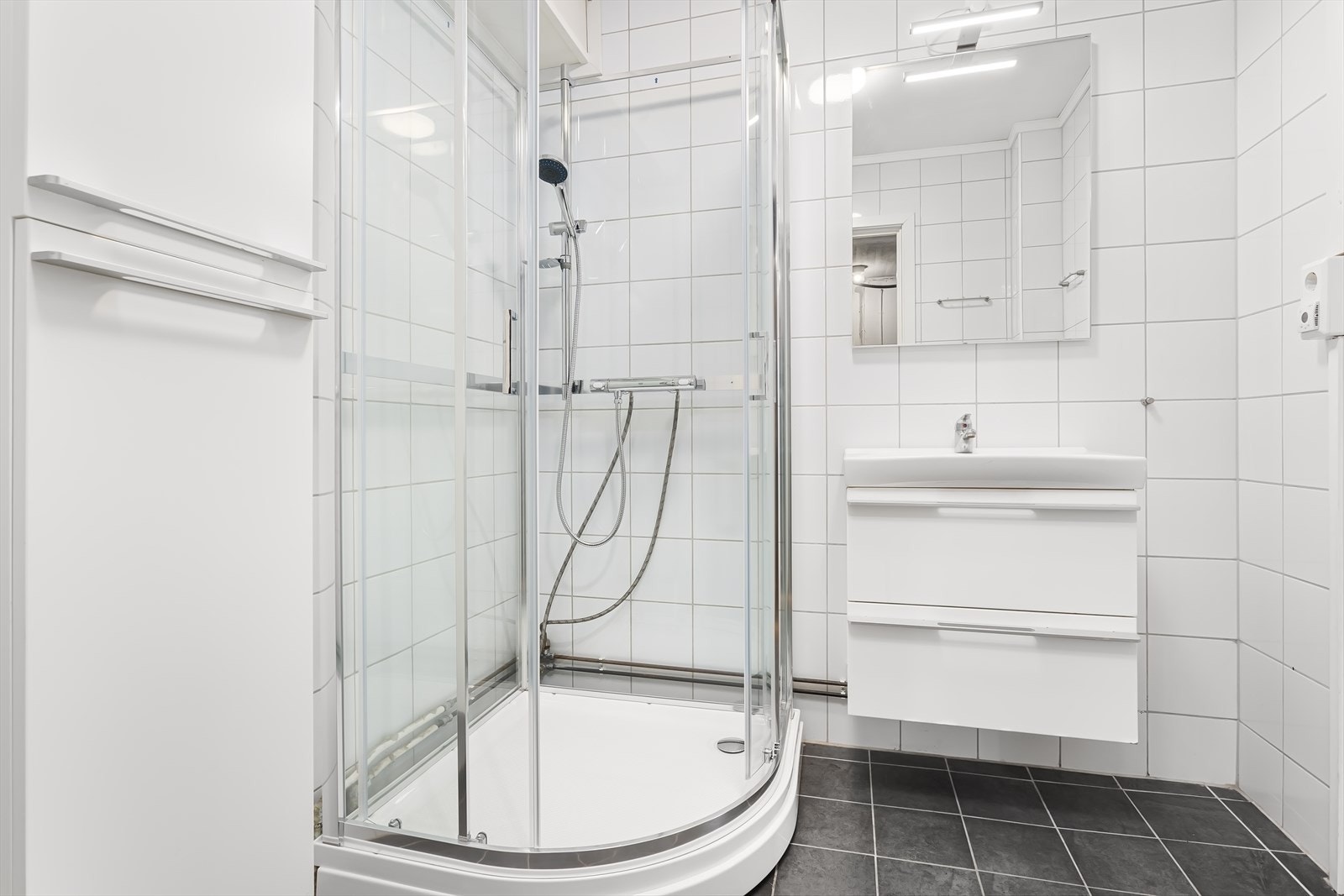 Badet er innredet med servant, speil med belysning, høyskap og dusjkabinett. Galleribilde