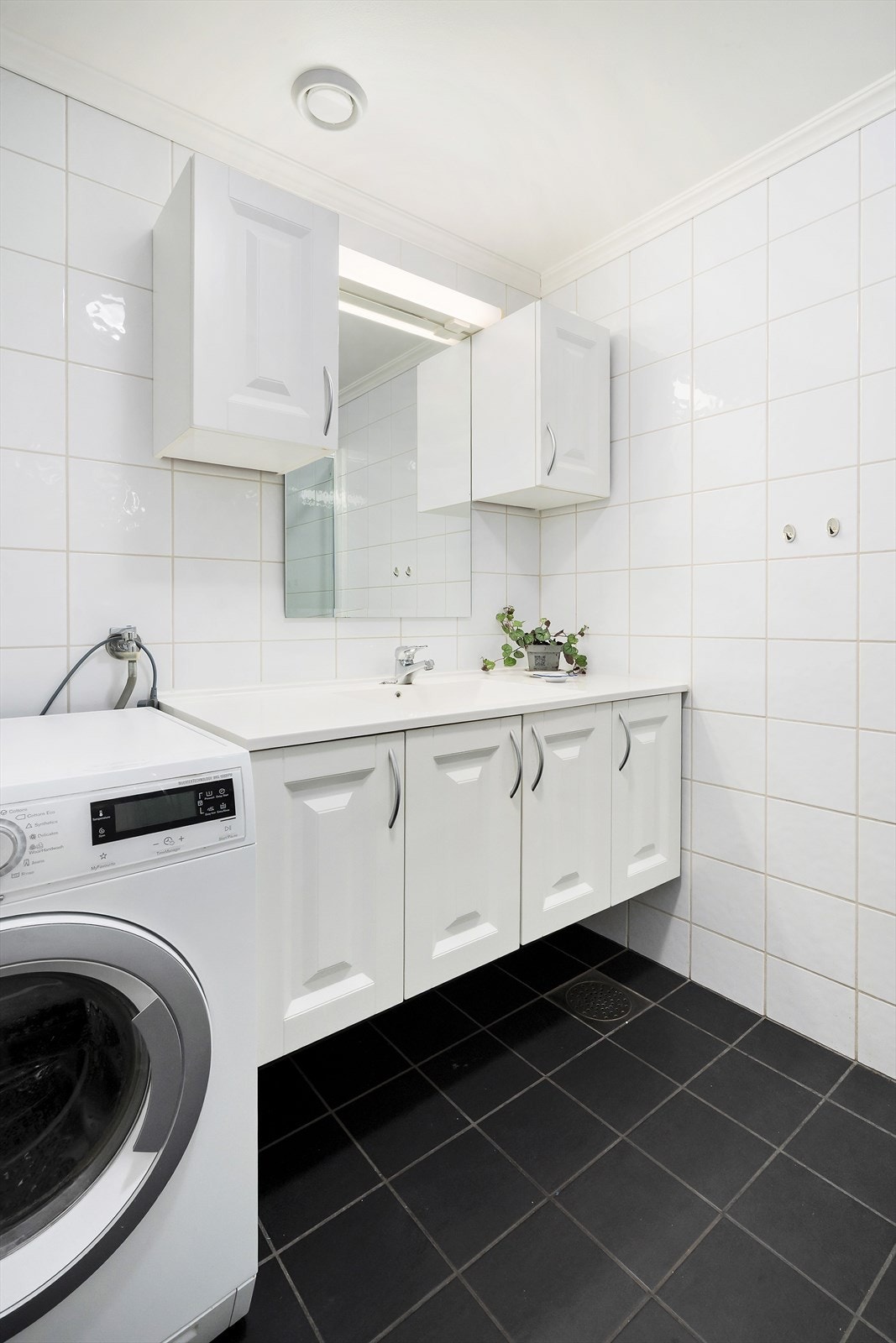 Pent flislagt bad med varmekabler. Hvit baderomsinnredning med servant og skap. Galleribilde