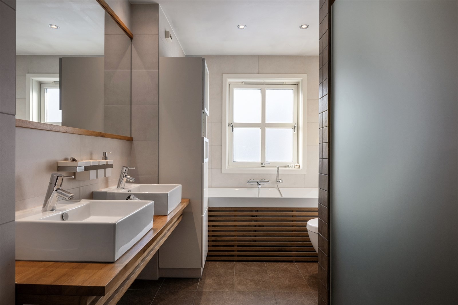 Her finner du moderne innredning med to nedfelte servanter, veggmontert toalett, dusjsluse og et avslappende badekar. Galleribilde