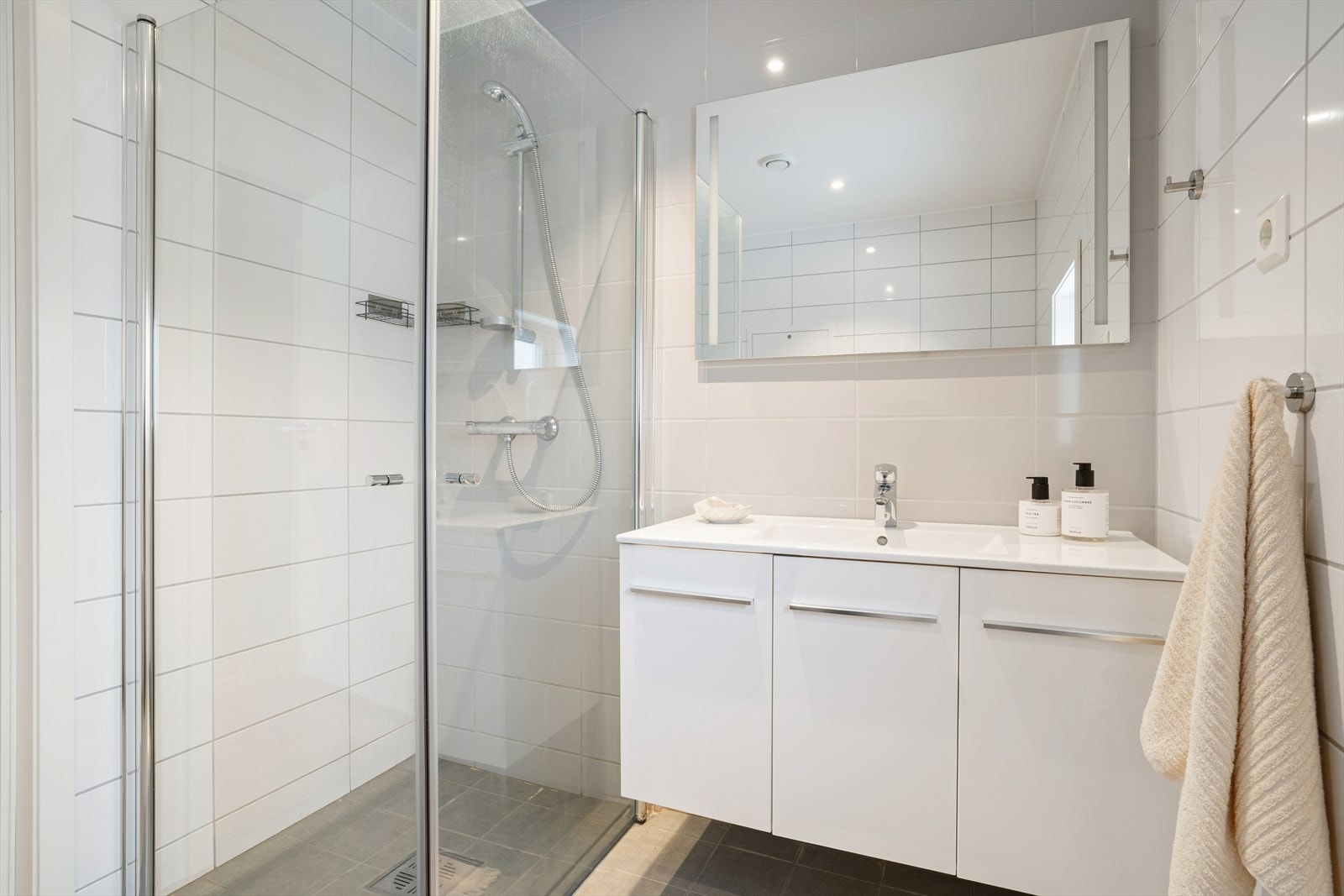 Rommet har flislagte vegger og gulv med elektriske varmekabler, vegghengt toalett, servant med innredning og dusjhjørne med glassvegger. Galleribilde