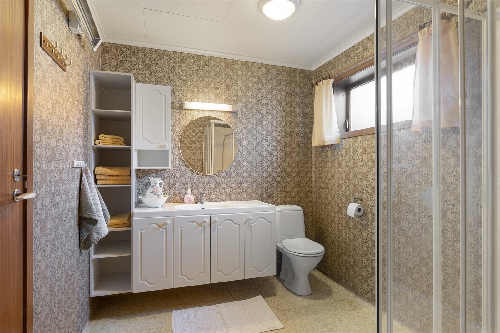 Baderommet i kjelleretasjen har våtromstapet på vegg og malte plater i tak. Våtromsbelegg på gulv. Rommet inneholder toalett på sokkel, seksjon med vask og tett dusjkabinett. Galleribilde