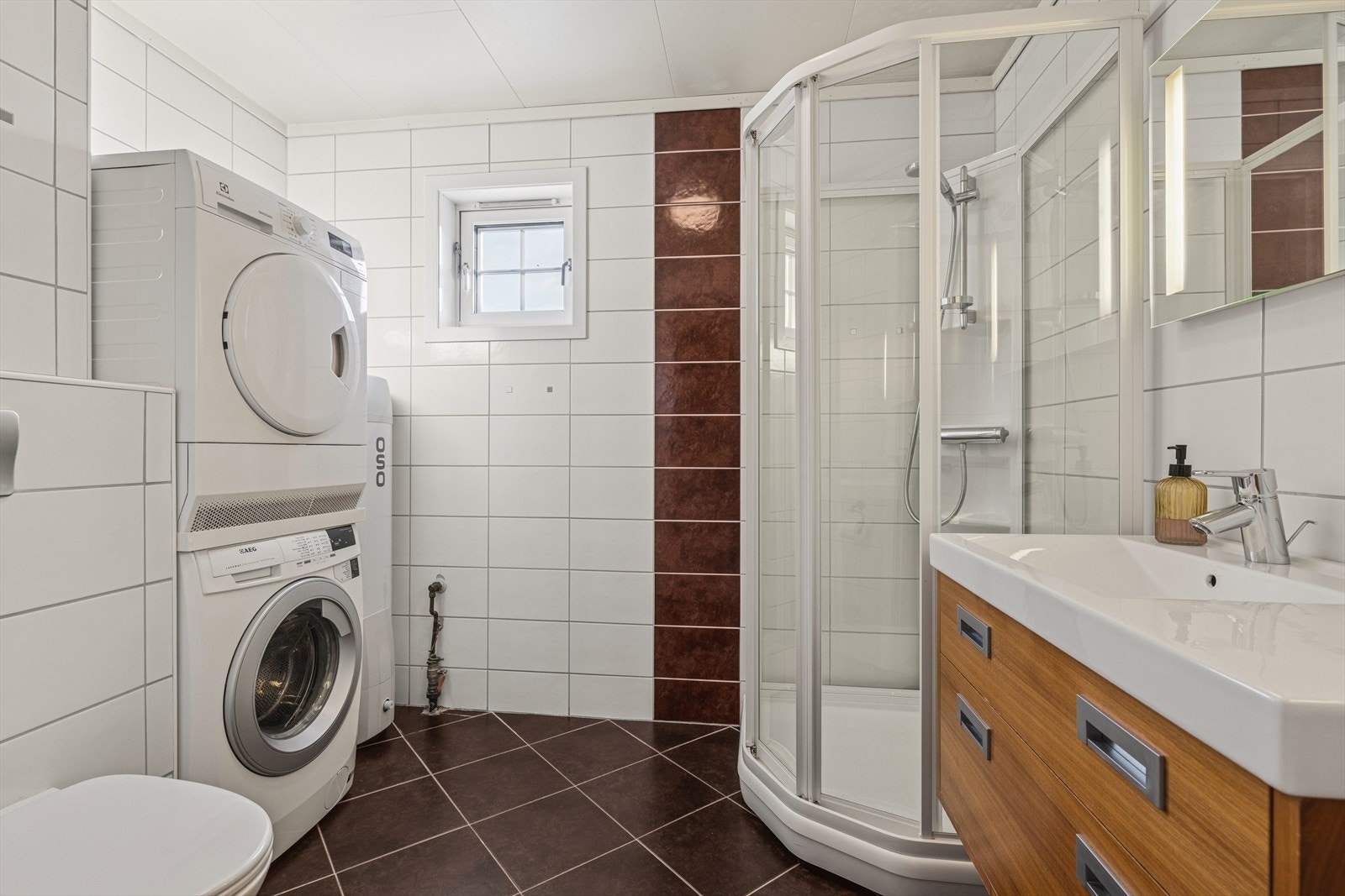 Bad i første etasje med flislagt gulv og vegger. Innredet med dusjkabinett, vegghengt toalett, opplegg til vaskemaskin og servant Galleribilde