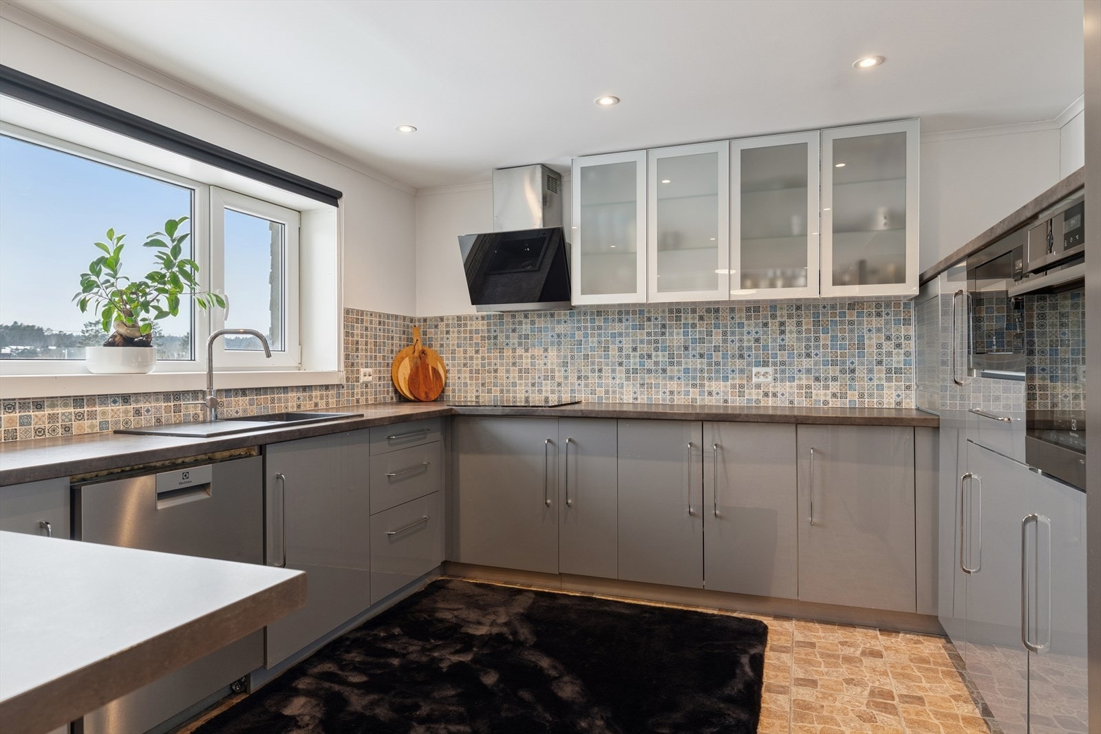 Kjøkkeninnredning fra 2020 med slette fronter og laminert benkeplate, utstyrt med komposittkum og ettgreps blandebatteri. Deler av veggflatene er flislagt. Galleribilde