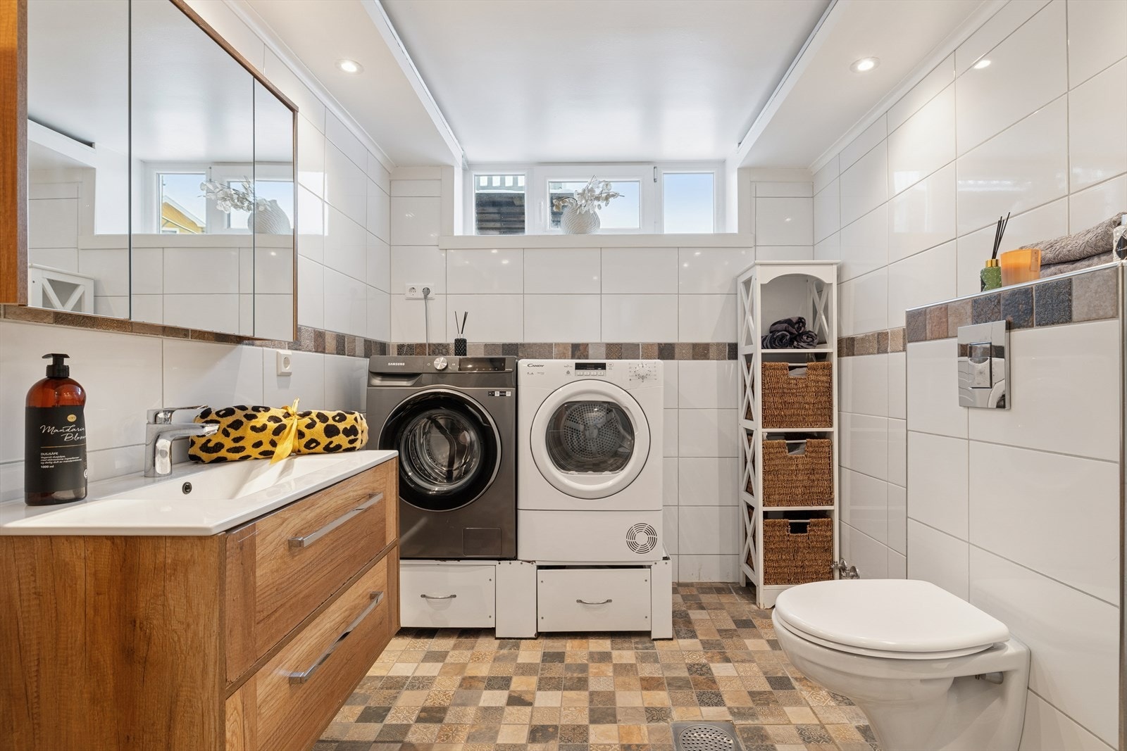 Flislagt baderom med innfelt belysning i himlingen, opplegg for vaskemaskin og plass til tørketrommel. Galleribilde