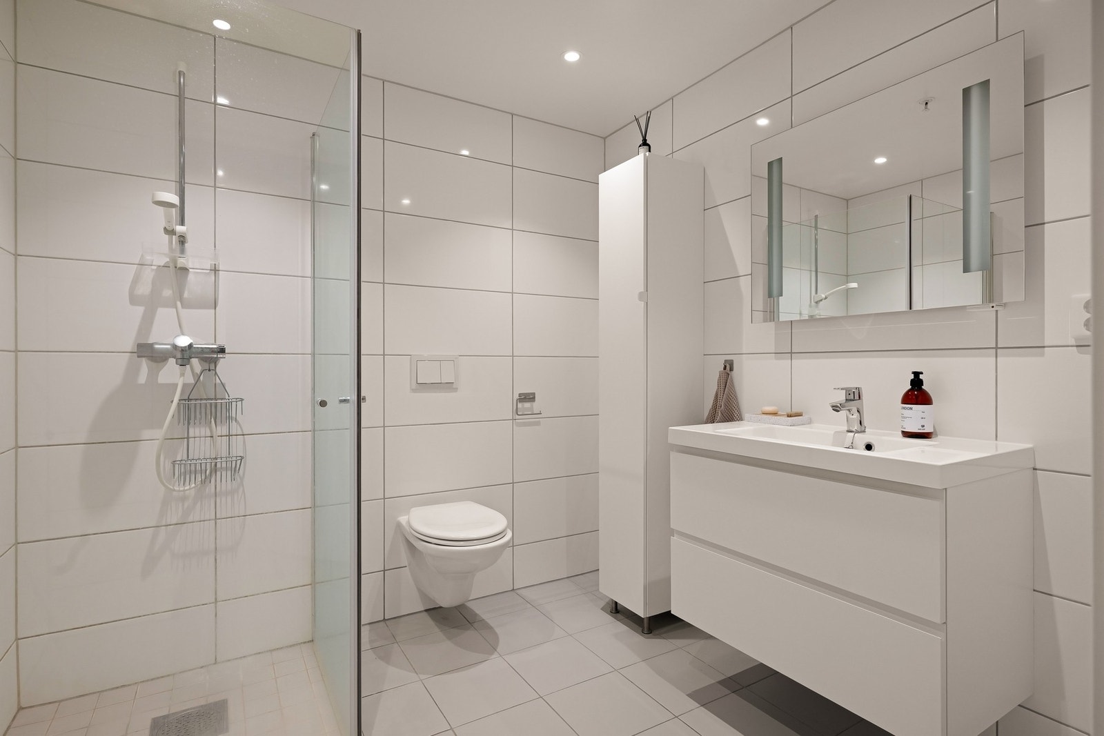 Badet er utstyrt med dusjhjørne, veggmontert wc, baderomsinnredning og speil med integrert belysning Galleribilde