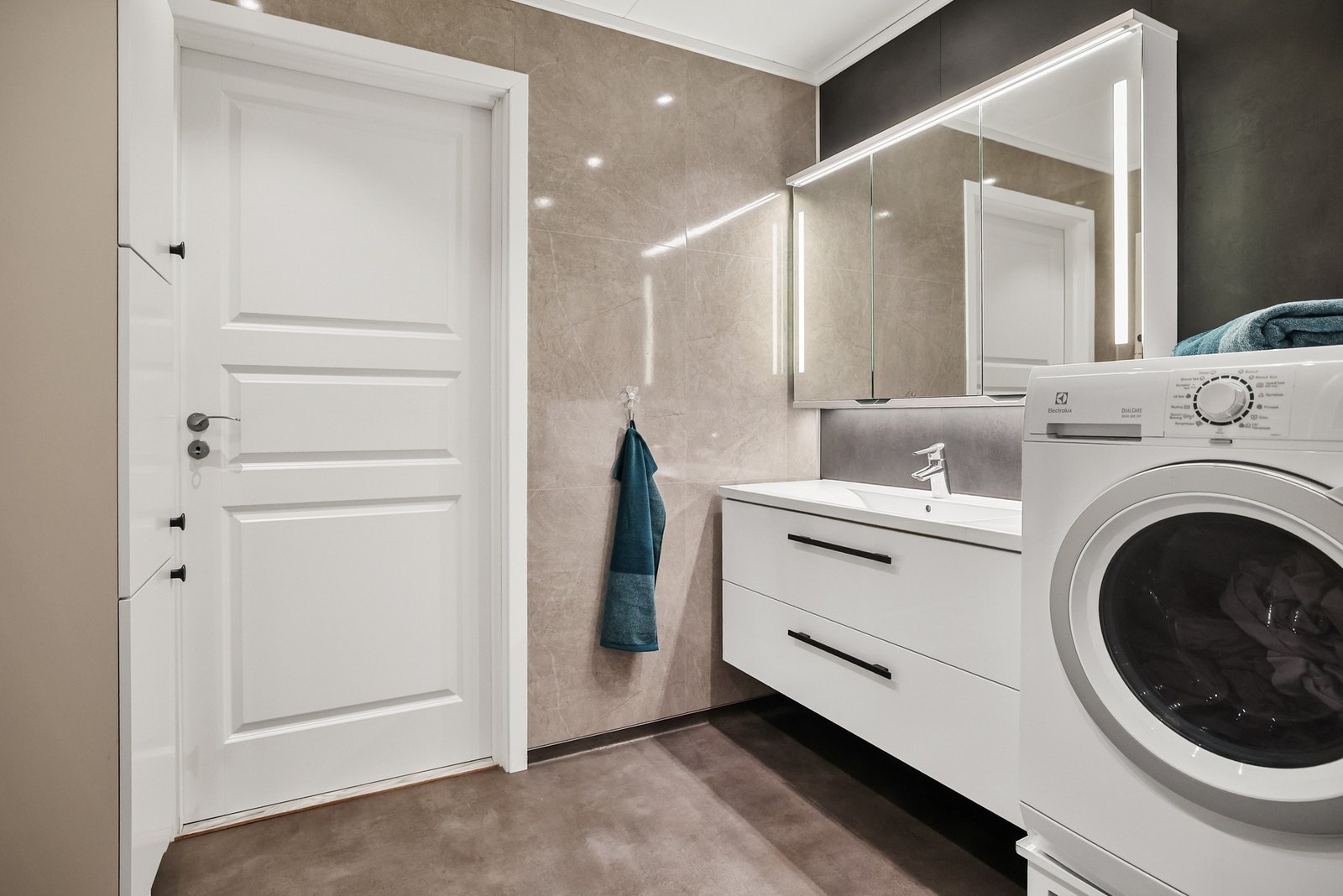 Baderommet inneholder dusjhjørne med dører, vegghengt toalett og opplegg for vaskemaskin. Galleribilde