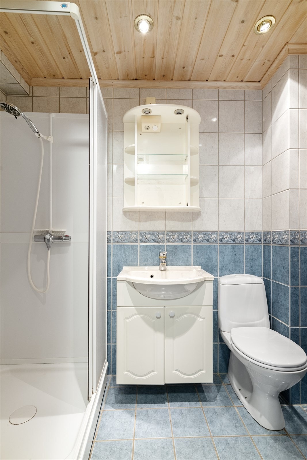 Flislagt bad med tilliggende vaskerom i 1. etasje. Badet er utstyrt med gulvmontert toalett, dusjkabinett og servantinnredning, samt downlights i tak. Galleribilde