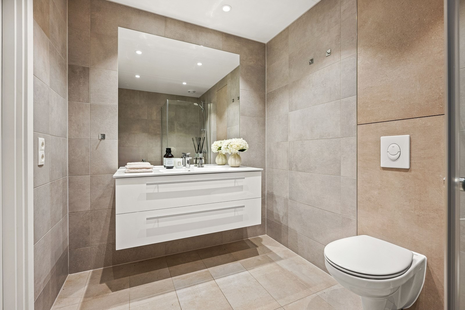 Delikat bad med stilrene, keramiske fliser på vegger og gulv, kombinert med innfelte LED-downlights i himlingen for optimal belysning. Galleribilde