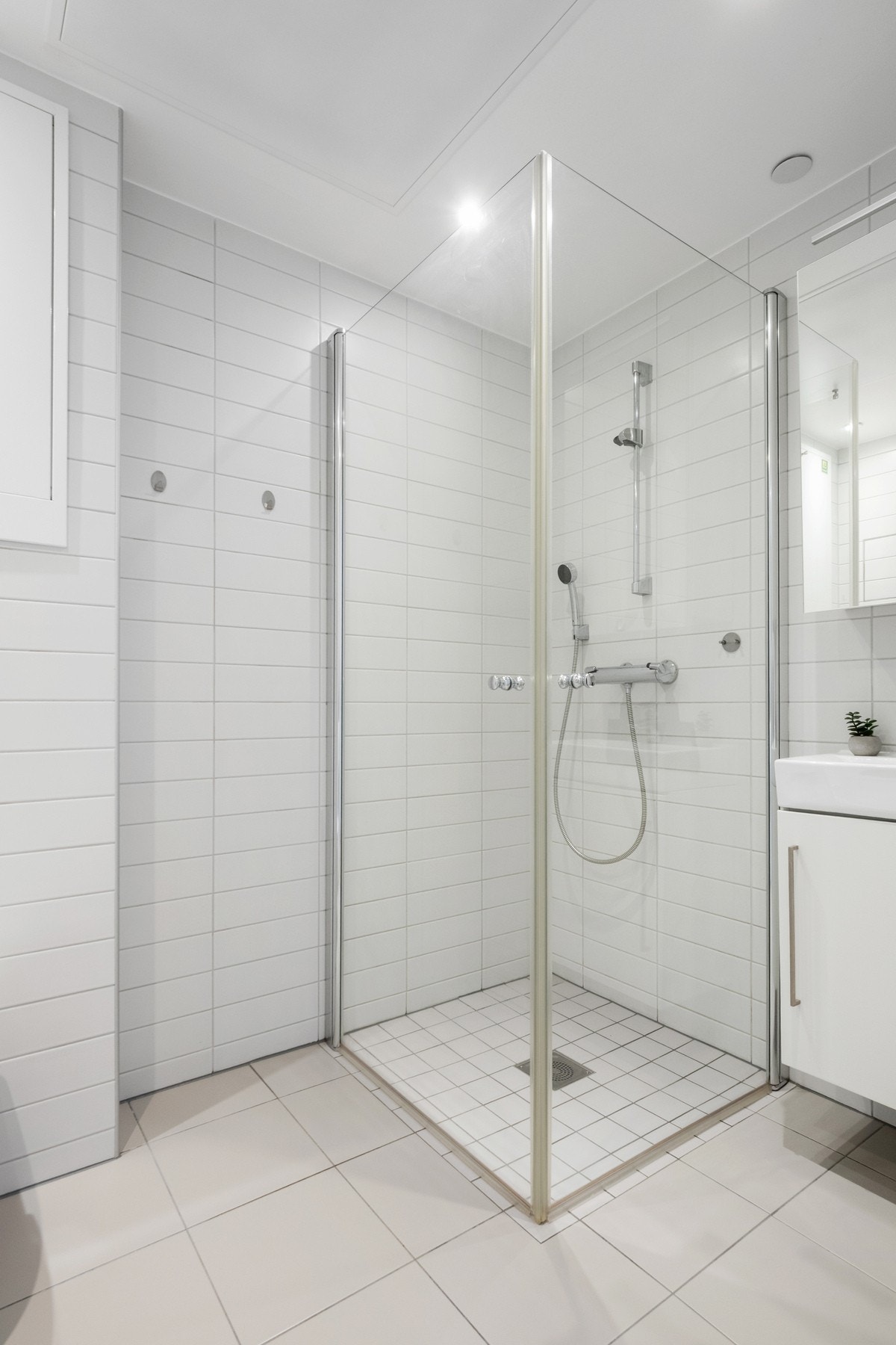 Gulvet er støpt og flislagt, med fall til sluk. Innredningen består av enkel servant, dusj med glassdører, veggmontert toalett og opplegg for vaskemaskin. Galleribilde