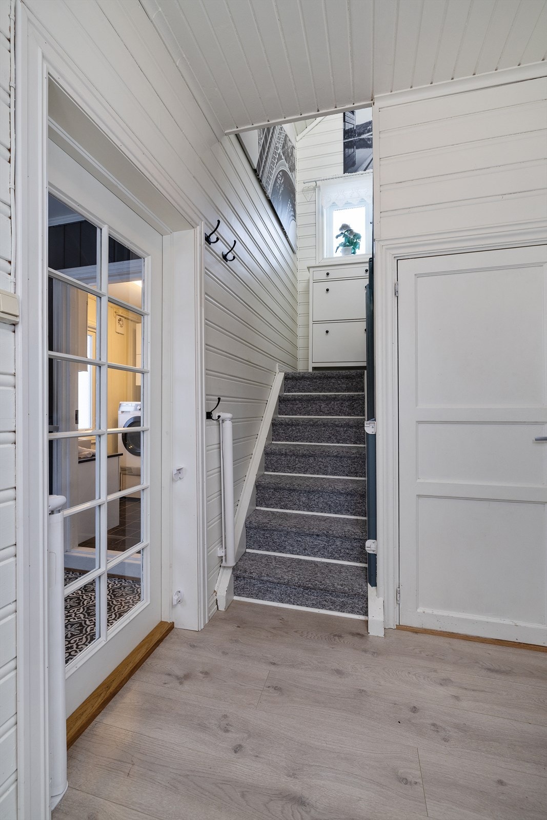 Den malte tretrappen med teppe i trinnene leder opp til boligens loftsetasje. Galleribilde