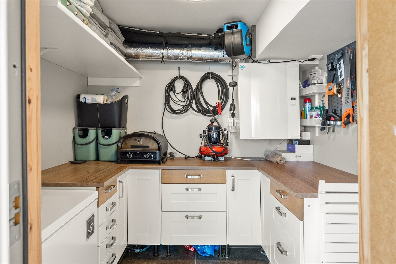 Boden på terrassen er innredet med skuffeseksjoner og arbeidsbenk. I tillegg har man strømuttak med plass til en ekstra fryser, samt hagemøbler og annet. Galleribilde