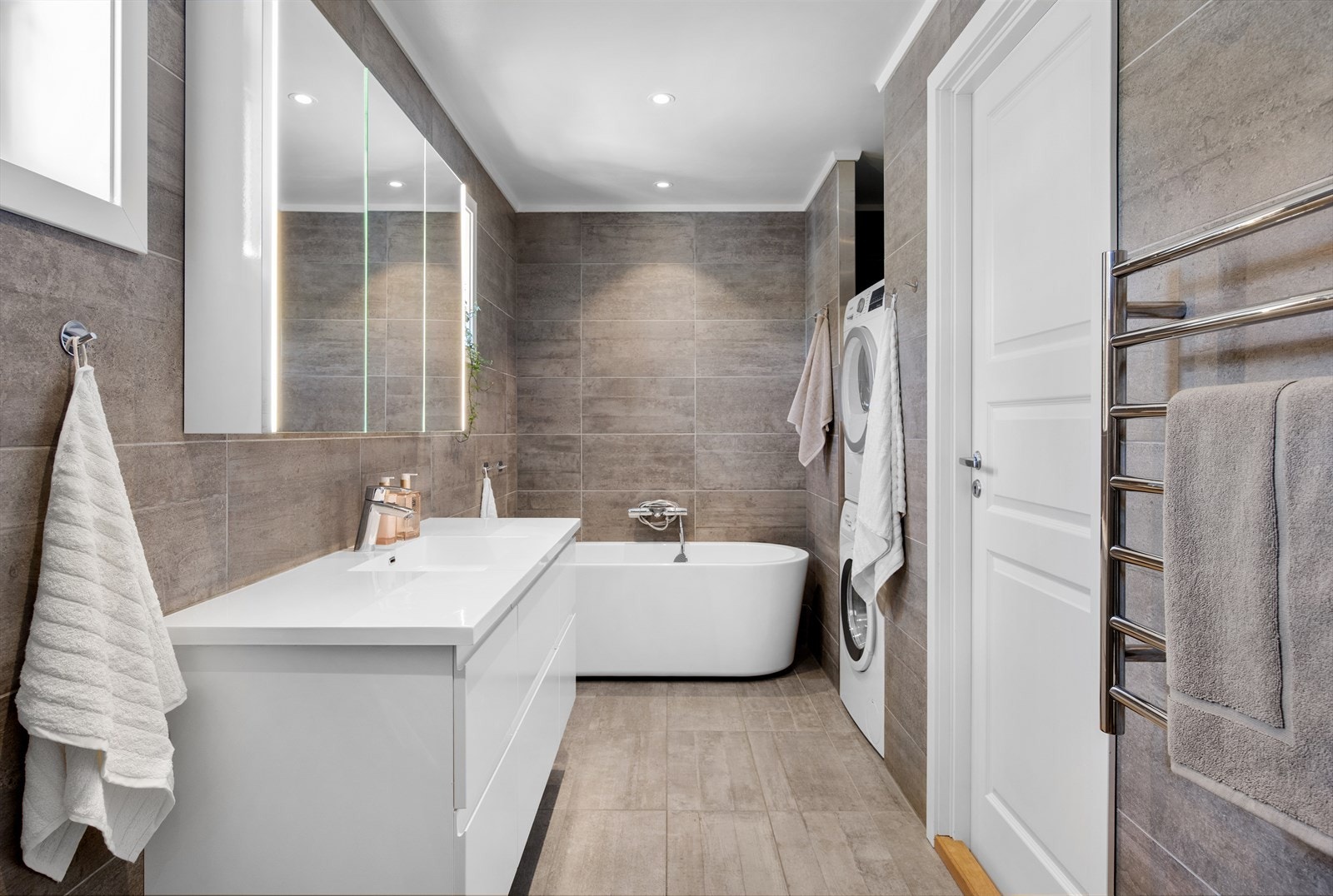 Flislagt baderom fra 2017. Badet har badekar med blandebatteri på vegg, servant med skuffer, speilskap med belysning og plassbygd vaskesøyle. Galleribilde