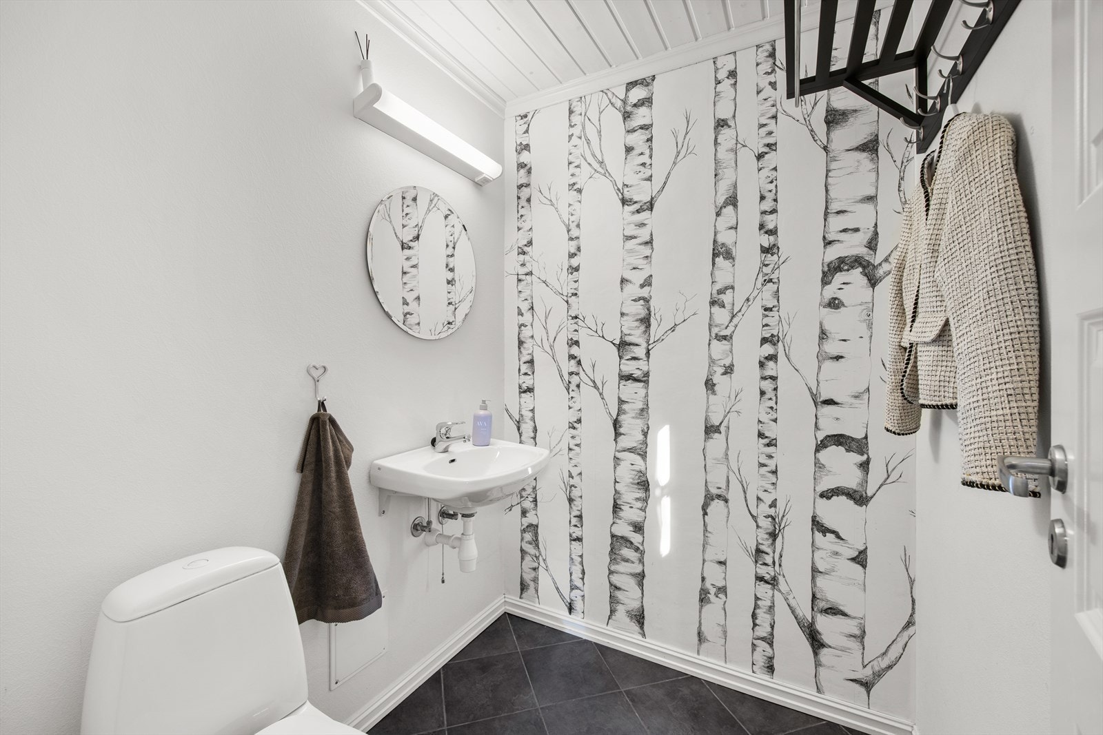 Toalettrom i første etasje med frittstående toalett, vask, speil og belysning. Galleribilde