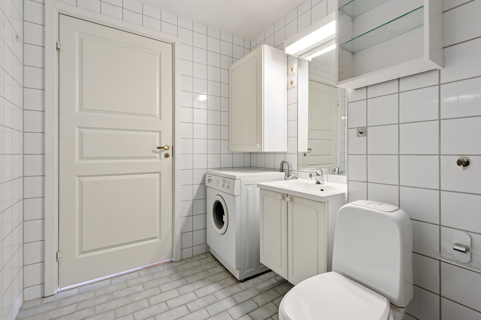 Badet er innredet med toalett, dusjkabinett, baderomsinnredning med servant, speil, flere veggskap og opplegg for vaskemaskin. Galleribilde