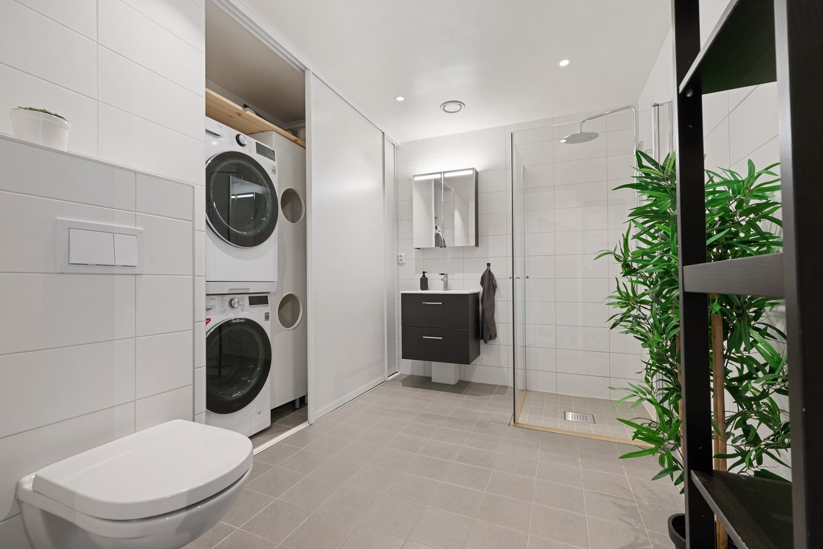 Lyst og romslig bad med vegghengt toalett, helservant på skuffeseksjon, speil med skapplass, og plass til vask/tørk Galleribilde