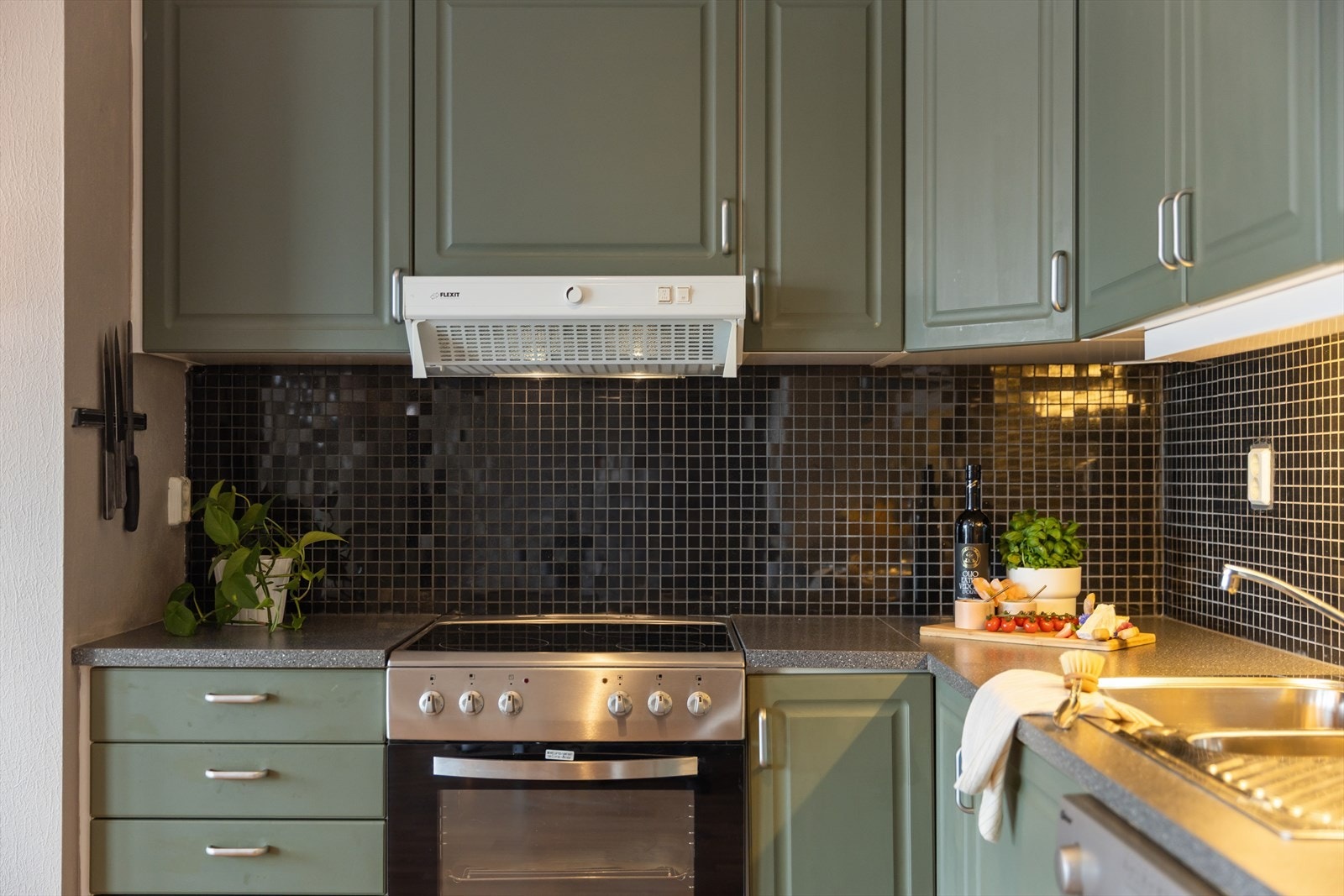 Lekre mosaikkfliser over benkeplatene. Kjøkkenventilator er av typen Flexit. Galleribilde