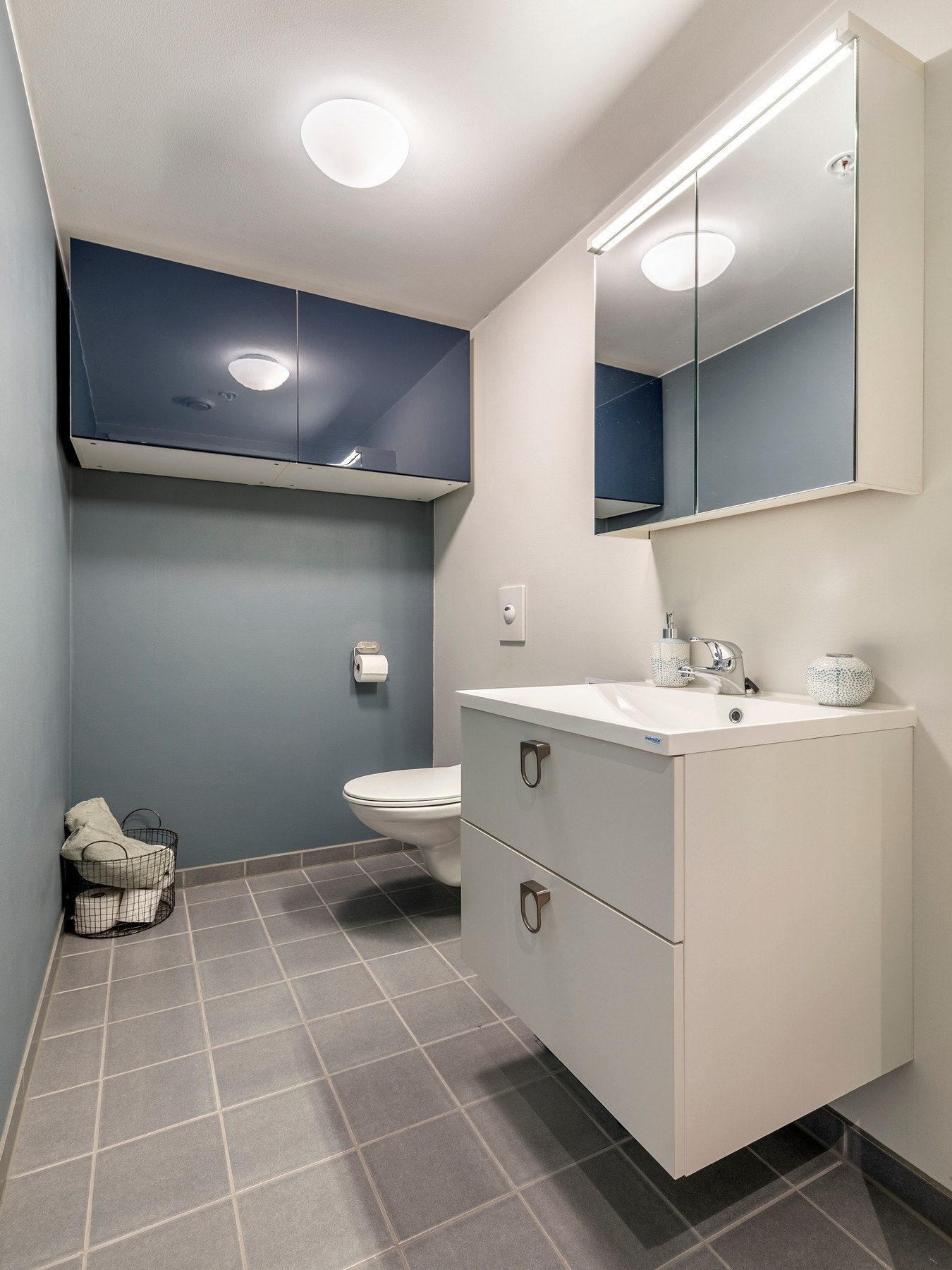 Toalettrommet har malte vegger og flislagt gulv - innredet med servantinnredning, skap på vegg og vegghengt toalett. Galleribilde