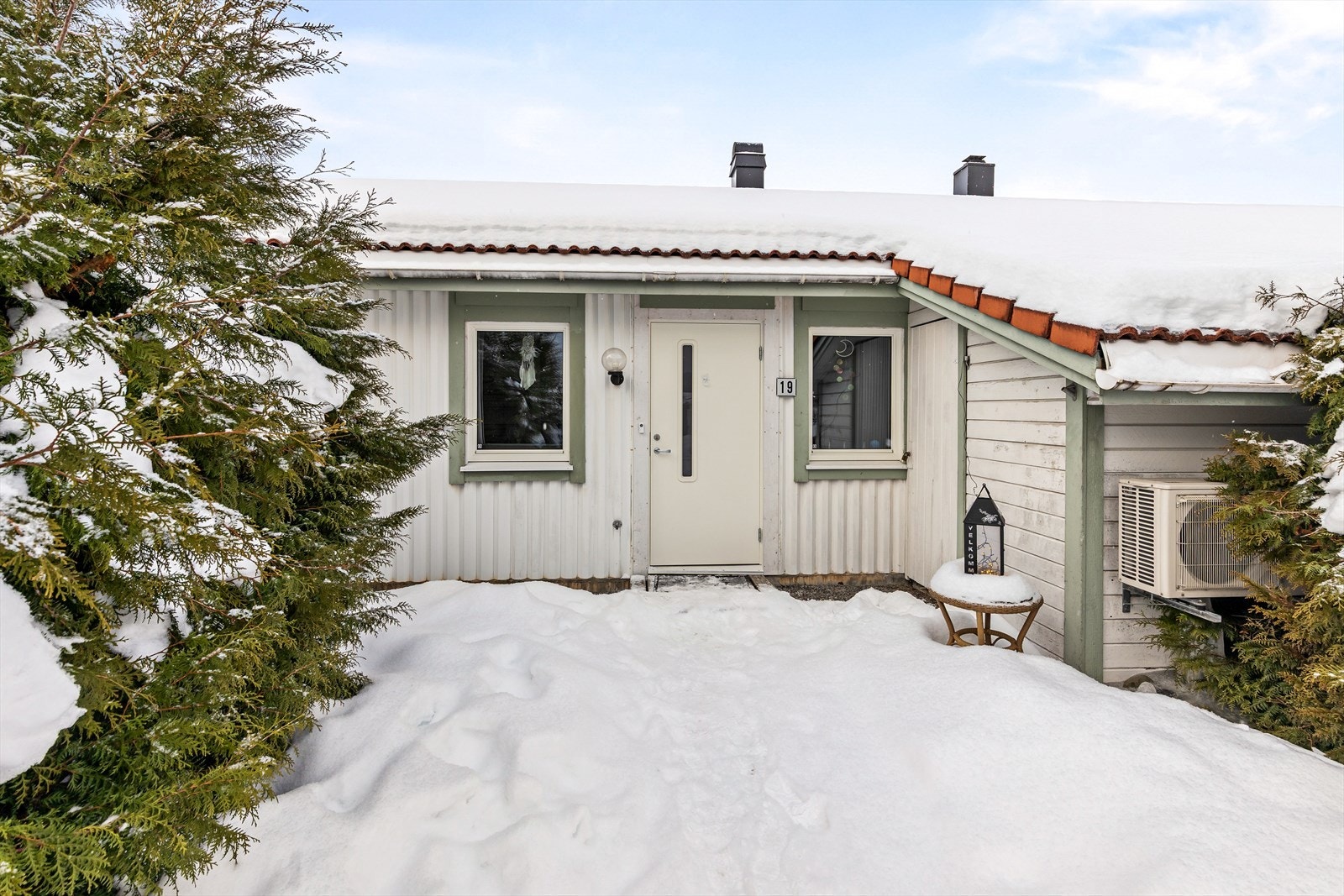 Usjenert inngangsparti med hekk på begge sider. Det er utebod ved inngangsdøren. Galleribilde