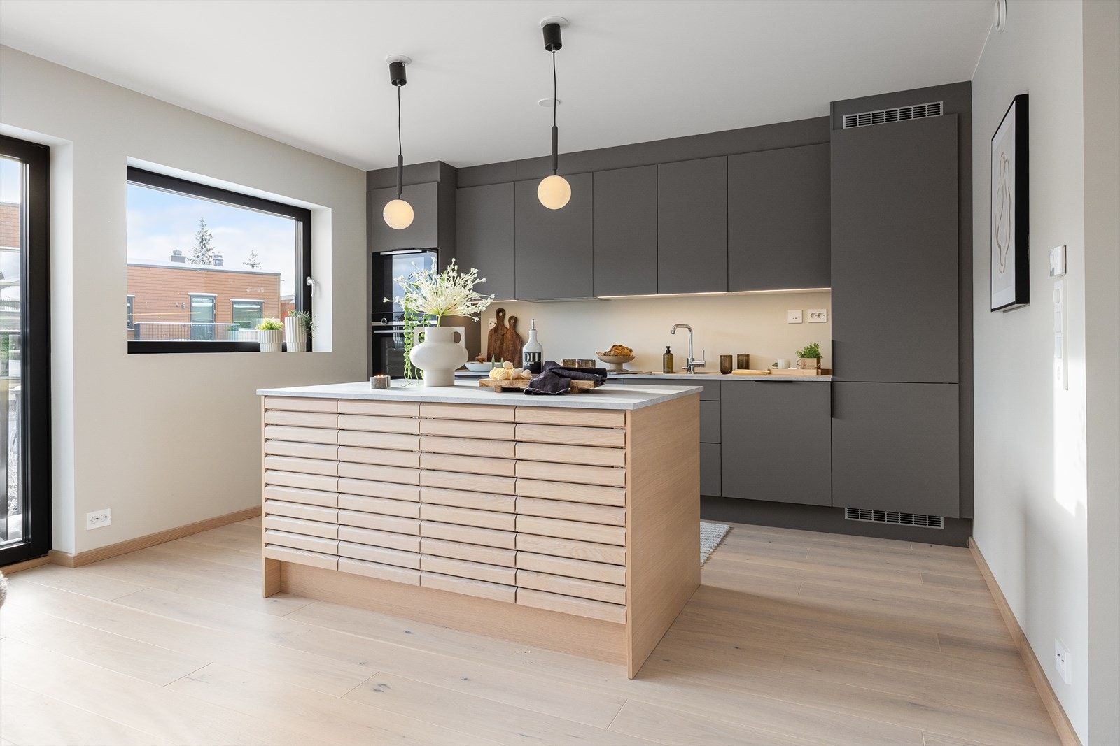 Innredningen langs veggen har takoppforede skap, matte fronter i fargen mørk sand og benkeplate med underlimt vaskekum. Galleribilde