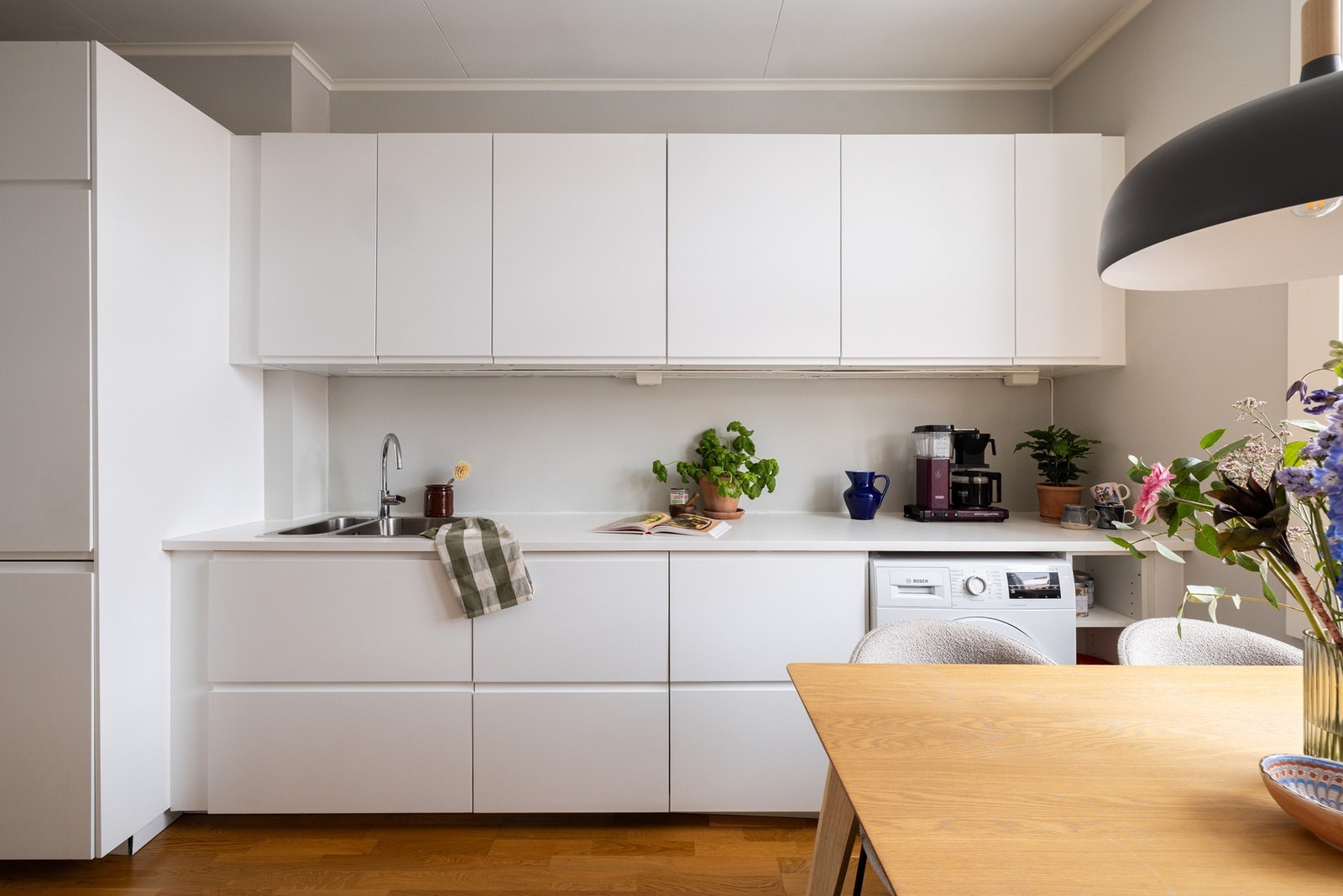 Det er svært god skap- og lagringsplass i kjøkkeninnredning med hvite glatte fronter og hvit laminat benkeplate. Galleribilde