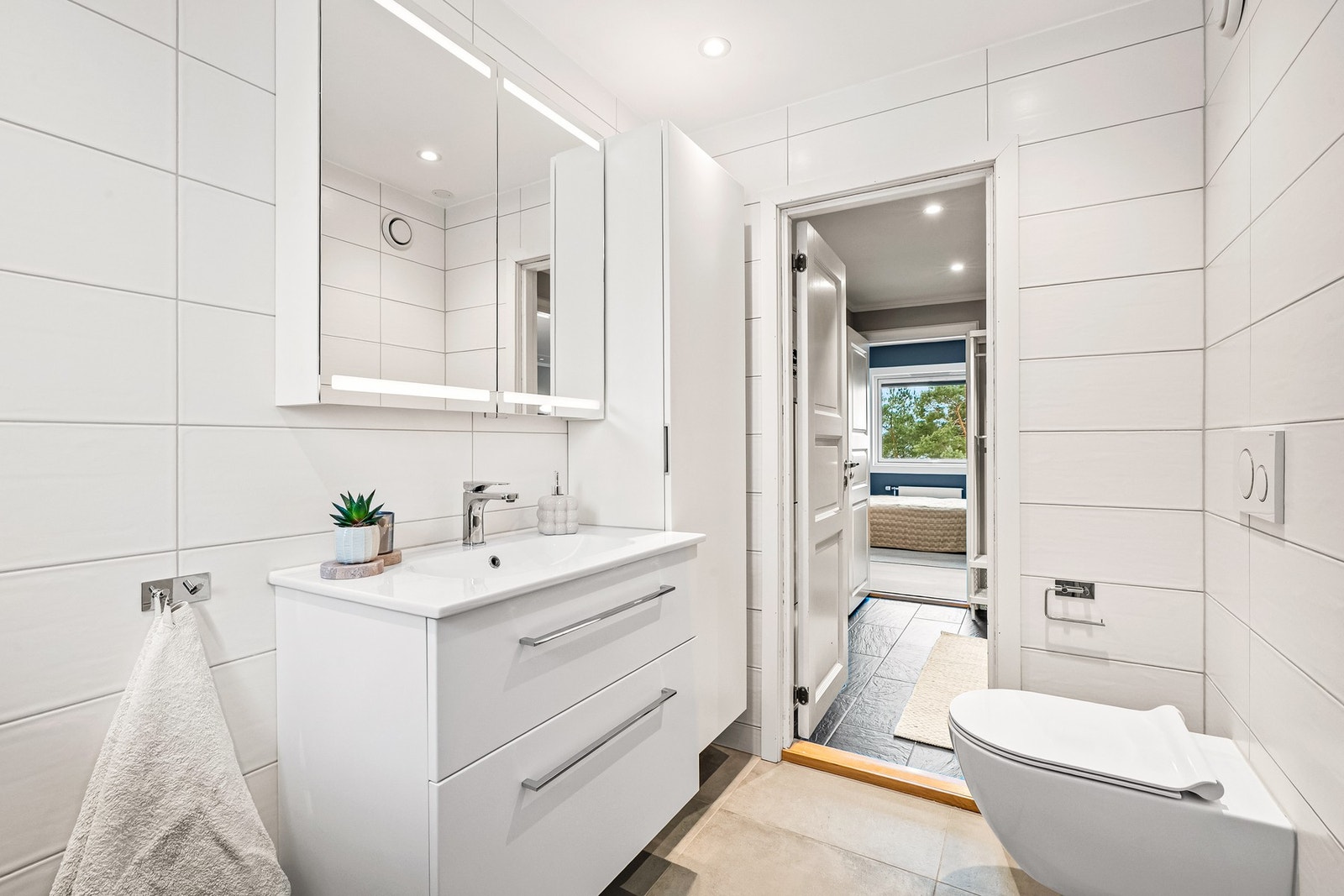 Badet er innredet med heldekkende servant og servantskap, vegghengt høyskap, vegghengt toalett, regnfallsdusj og opplegg for vaskemaskin. Galleribilde