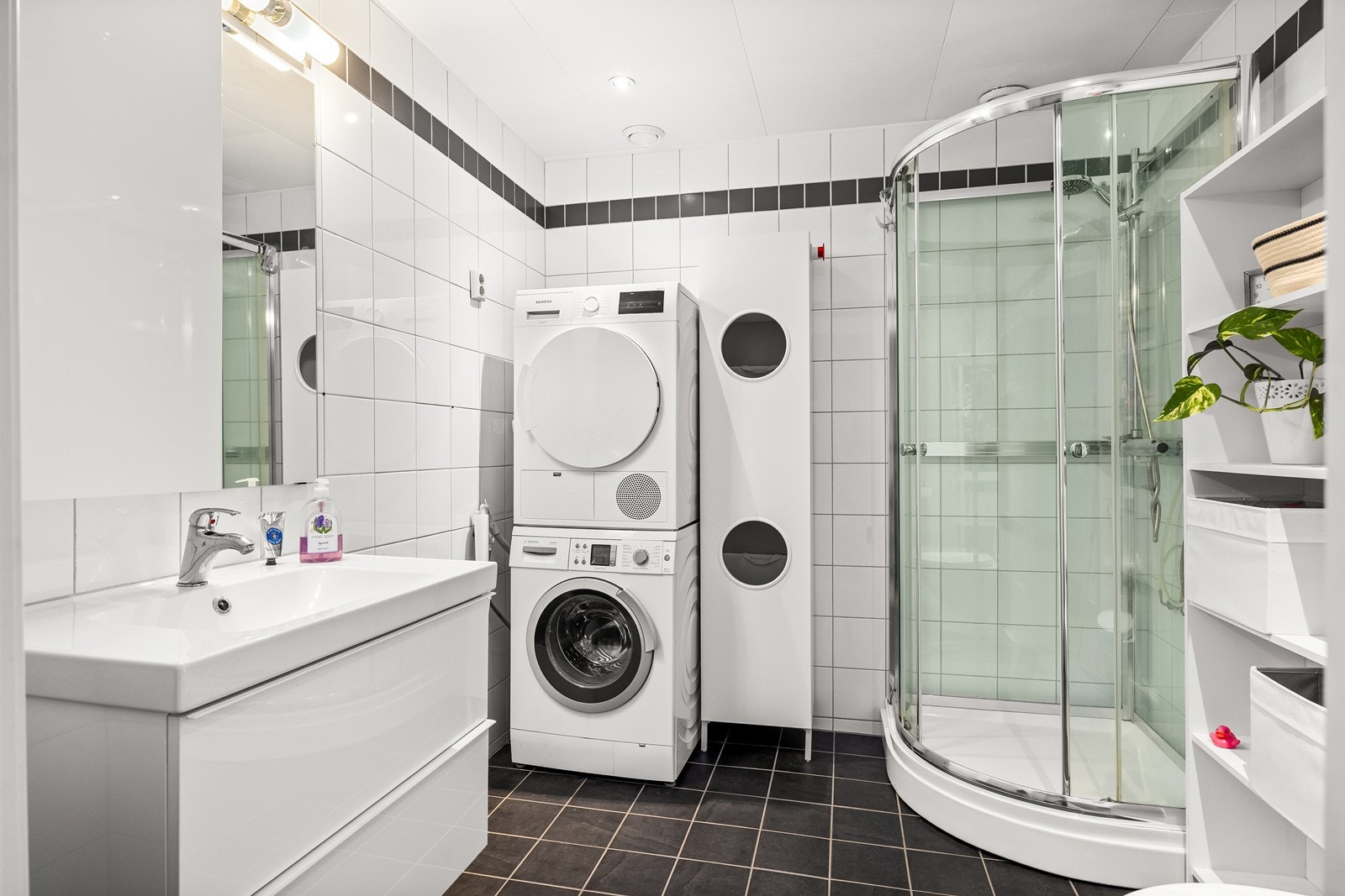 Flislagte vegger og gulv gir et moderne uttrykk, mens opplegg til vaskemaskin og tørketrommel sikrer praktisk funksjonalitet. Galleribilde