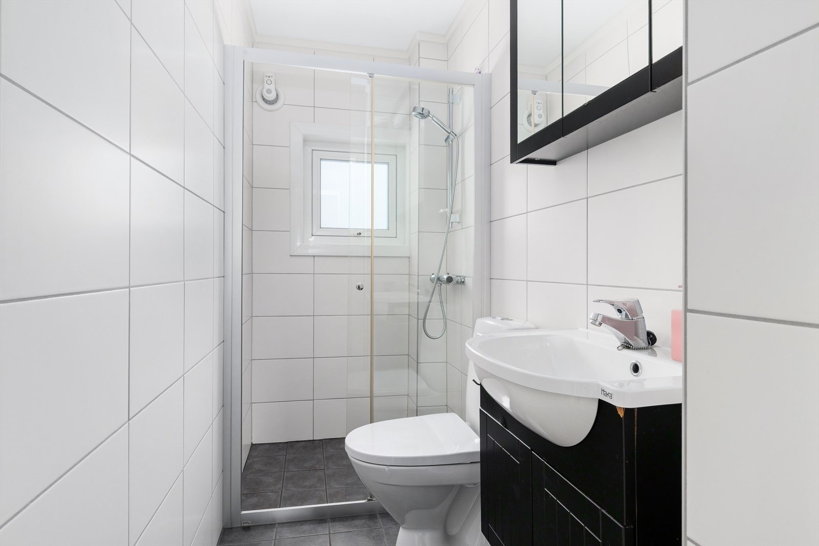 Pent flislagt bad med dusjnisje, wc og servant med praktisk innredning. Galleribilde