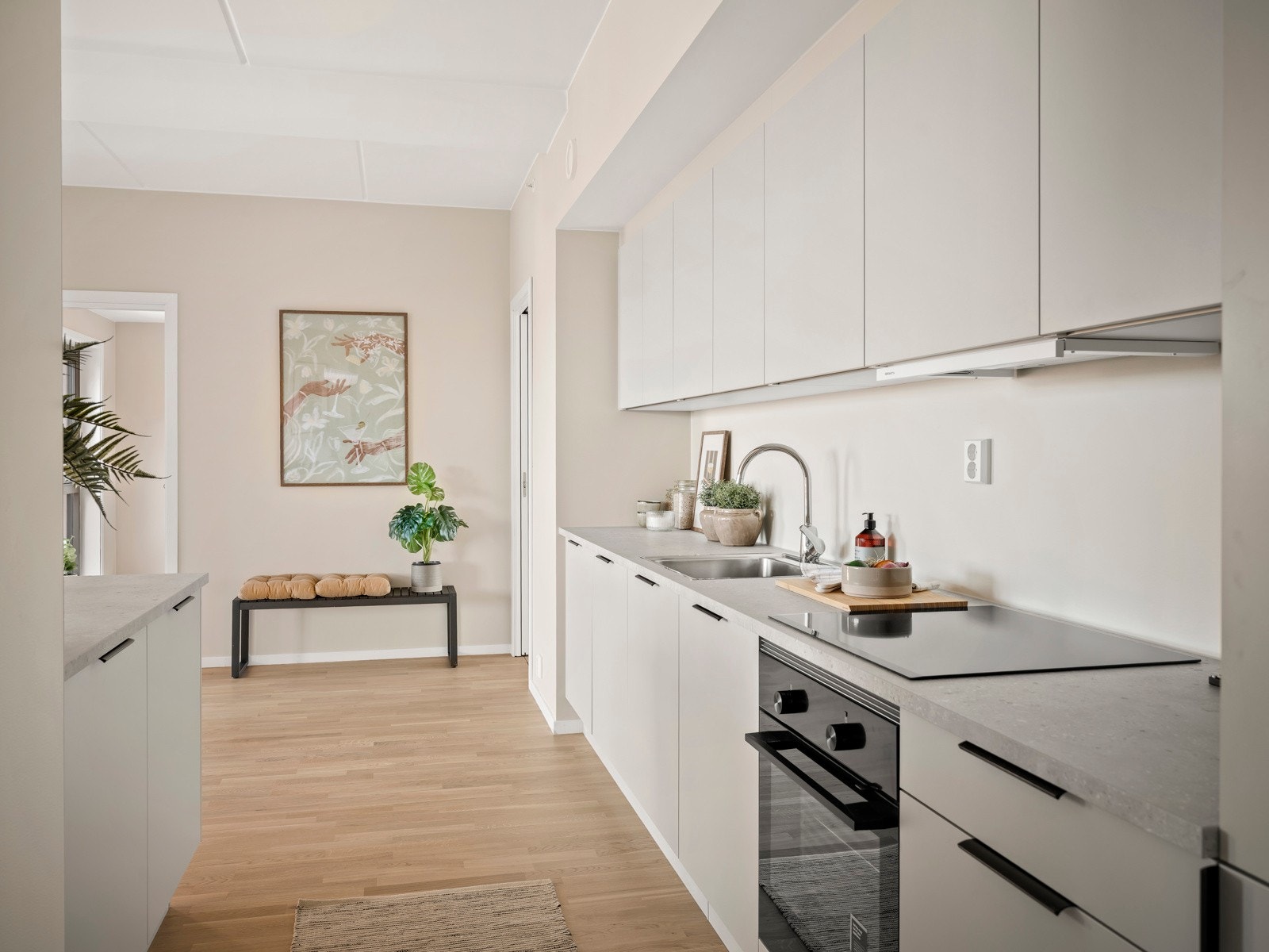 Kjøkkenet har beige slette fronter, håndtak i eloxert brun, nedfelt vask av typen Intra Omnia 600 SF Stålkum, blandebatteri av typen Damixa Rowan i rustfritt stål, og laminert benkeplate i fargen Sandsten. Galleribilde